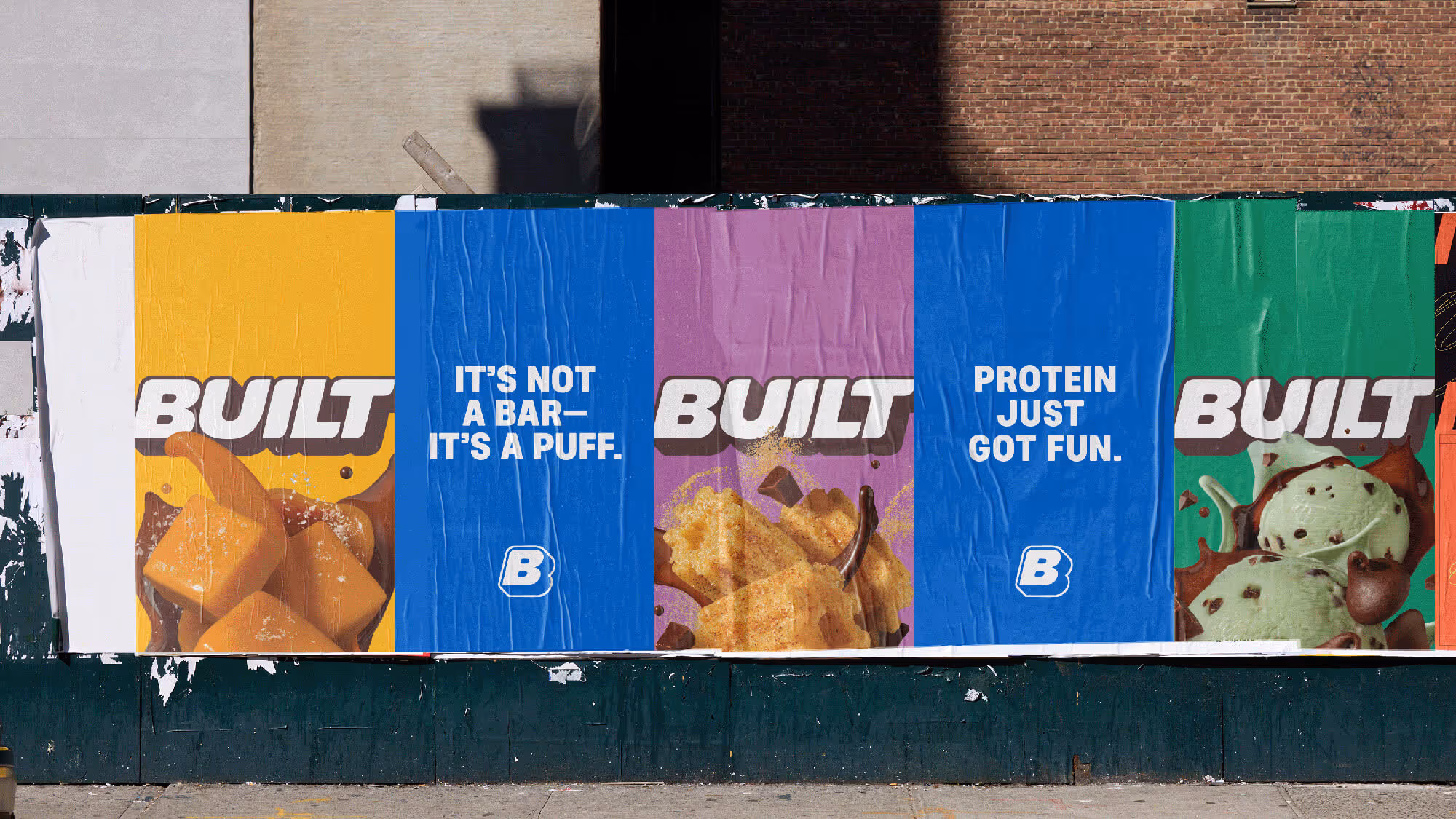 Row of yellow, blue, purple, and green Built posters wheatpasted on a brick city wall.