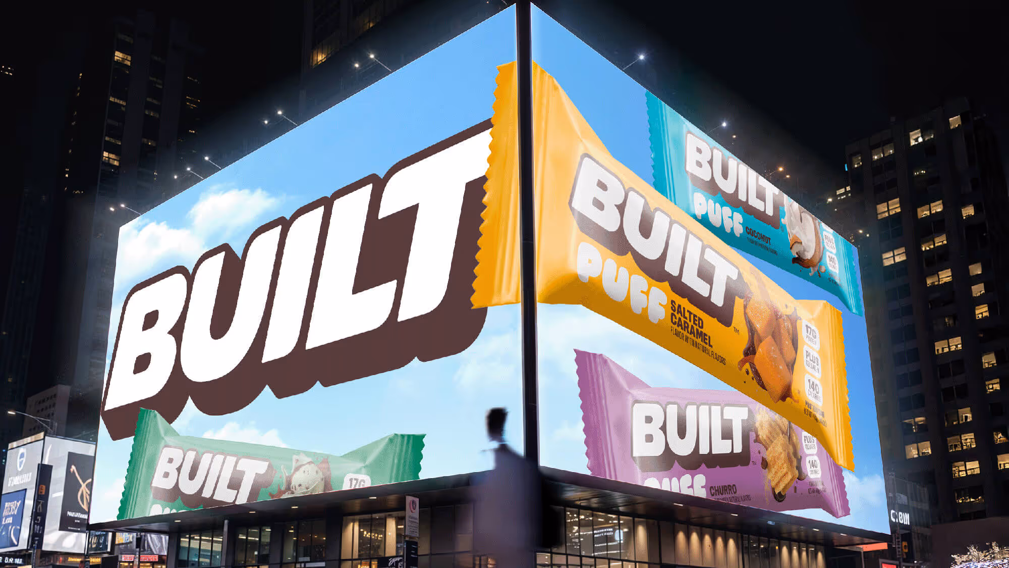 Nighttime city corner billboard with oversized Built Puff bar wrappers in yellow, teal, green, and purple.
