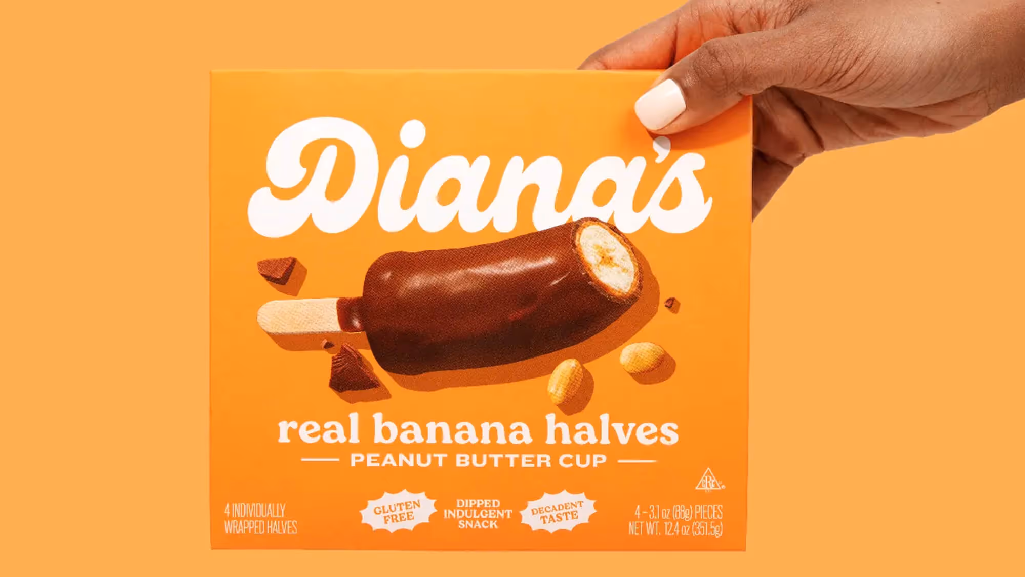 Hand with white nails holding an orange Diana's Peanut Butter Cup box on matching orange.