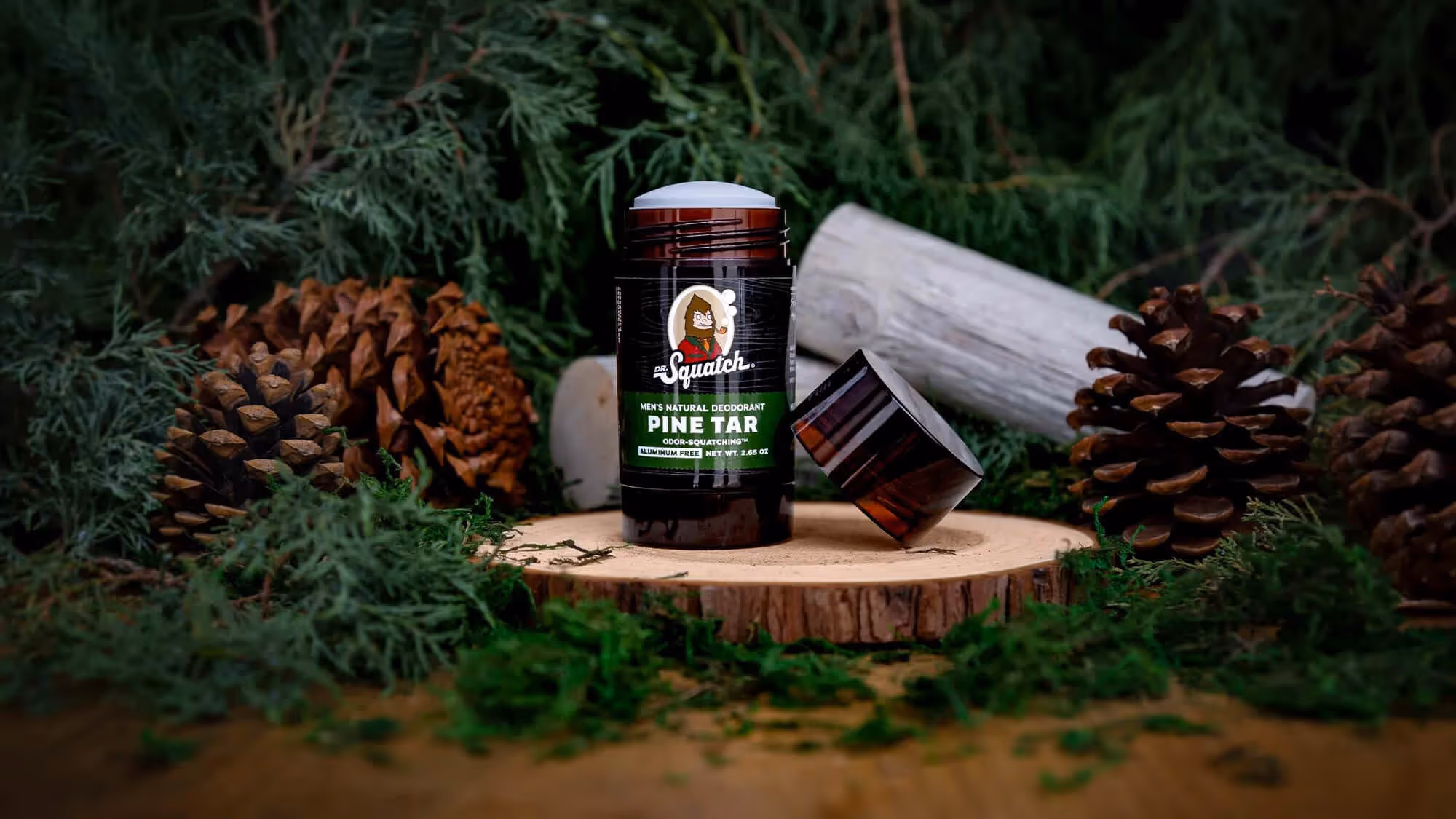Uncapped Dr. Squatch Pine Tar deodorant on a wood slice with moss and pine cones.