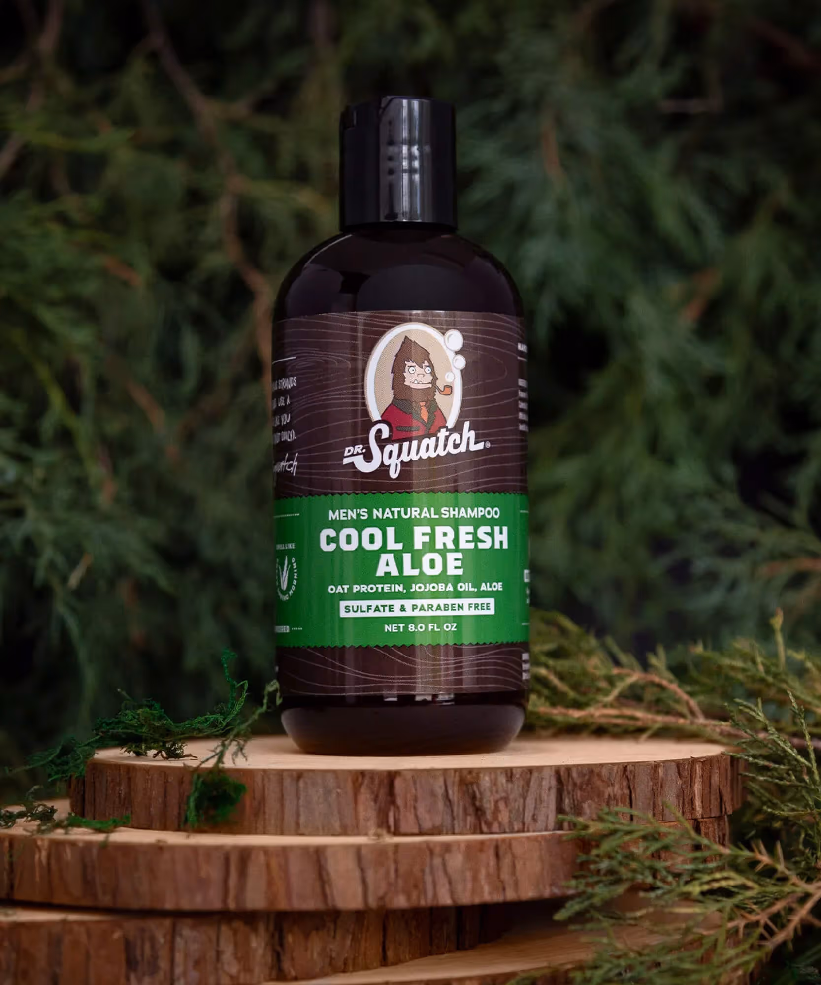 Dr. Squatch Cool Fresh Aloe shampoo bottle on stacked wood slices with cedar foliage.