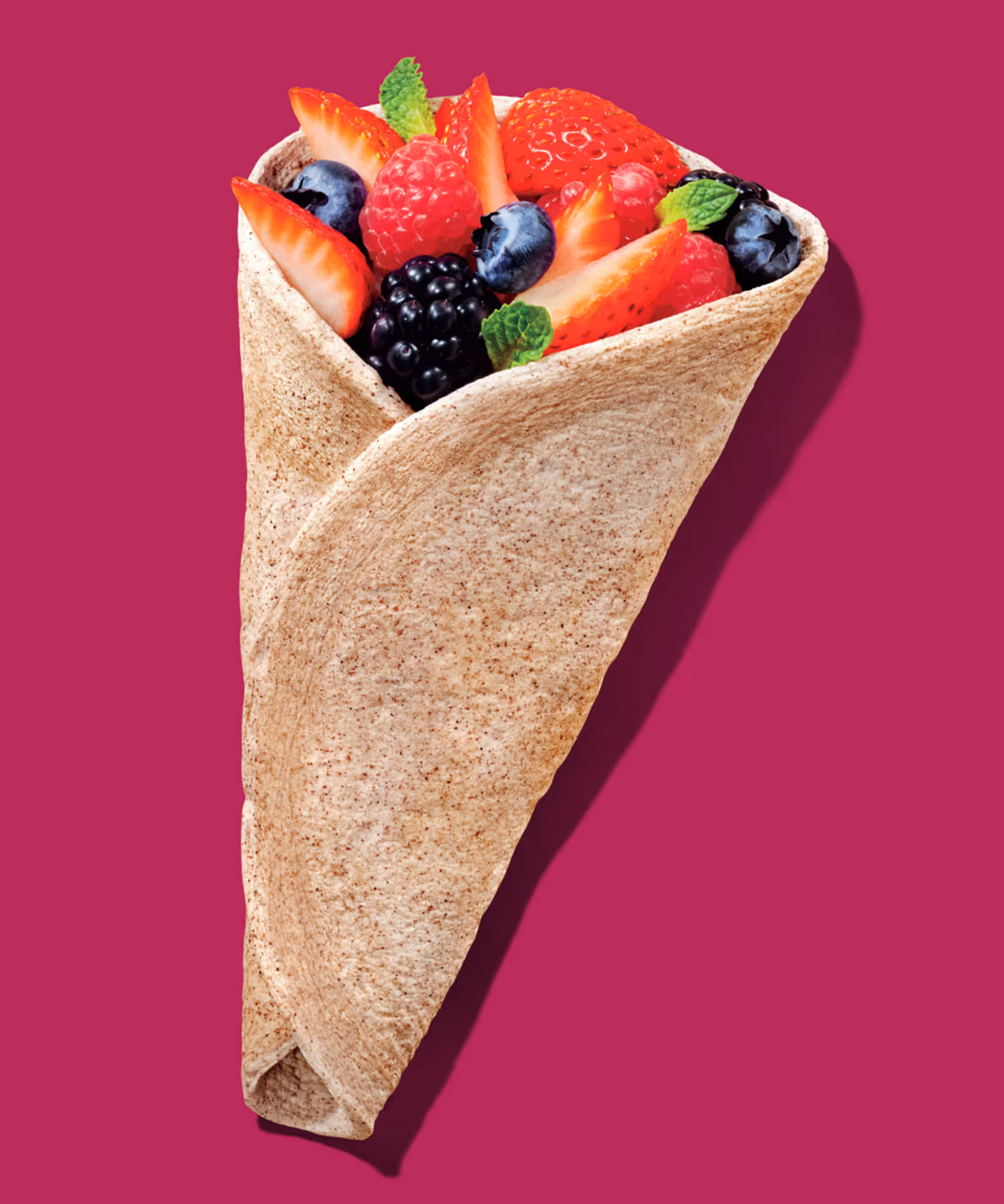Tan egg-white wrap filled with strawberries, blackberries, blueberries, and mint on a magenta background.