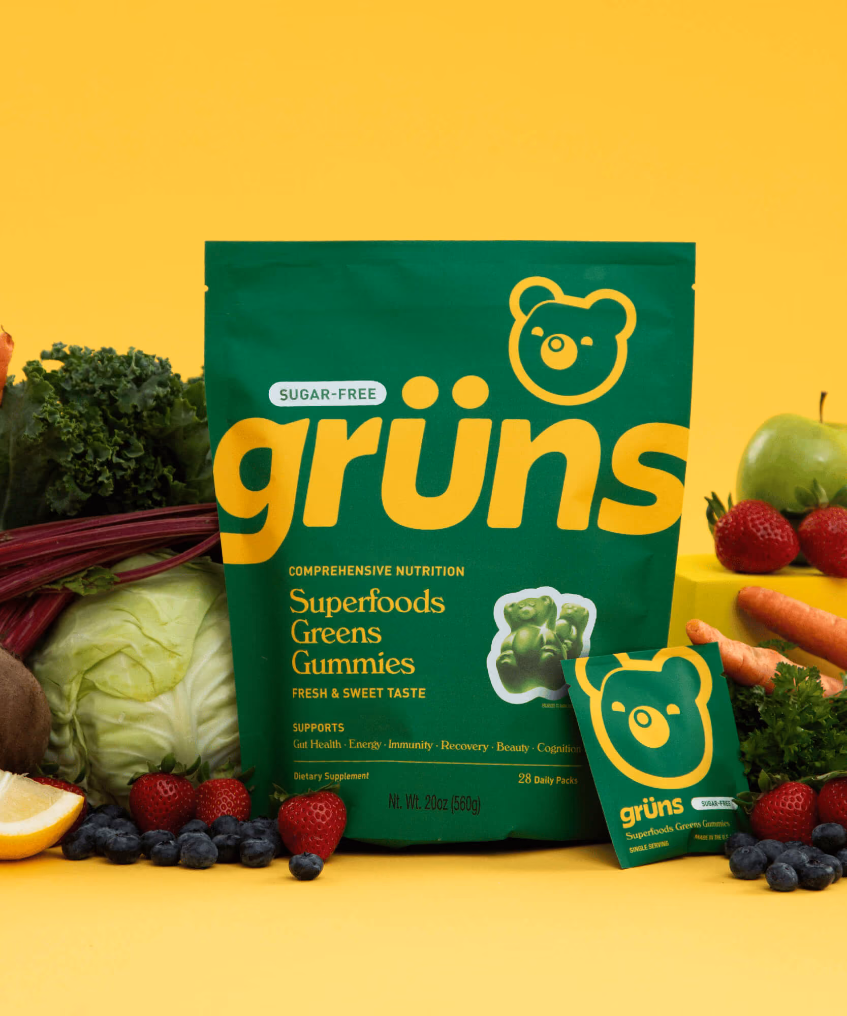 Green Grüns Greens Gummies pouch surrounded by carrots, kale, beets, kiwi, lemon, strawberries, and parsley.