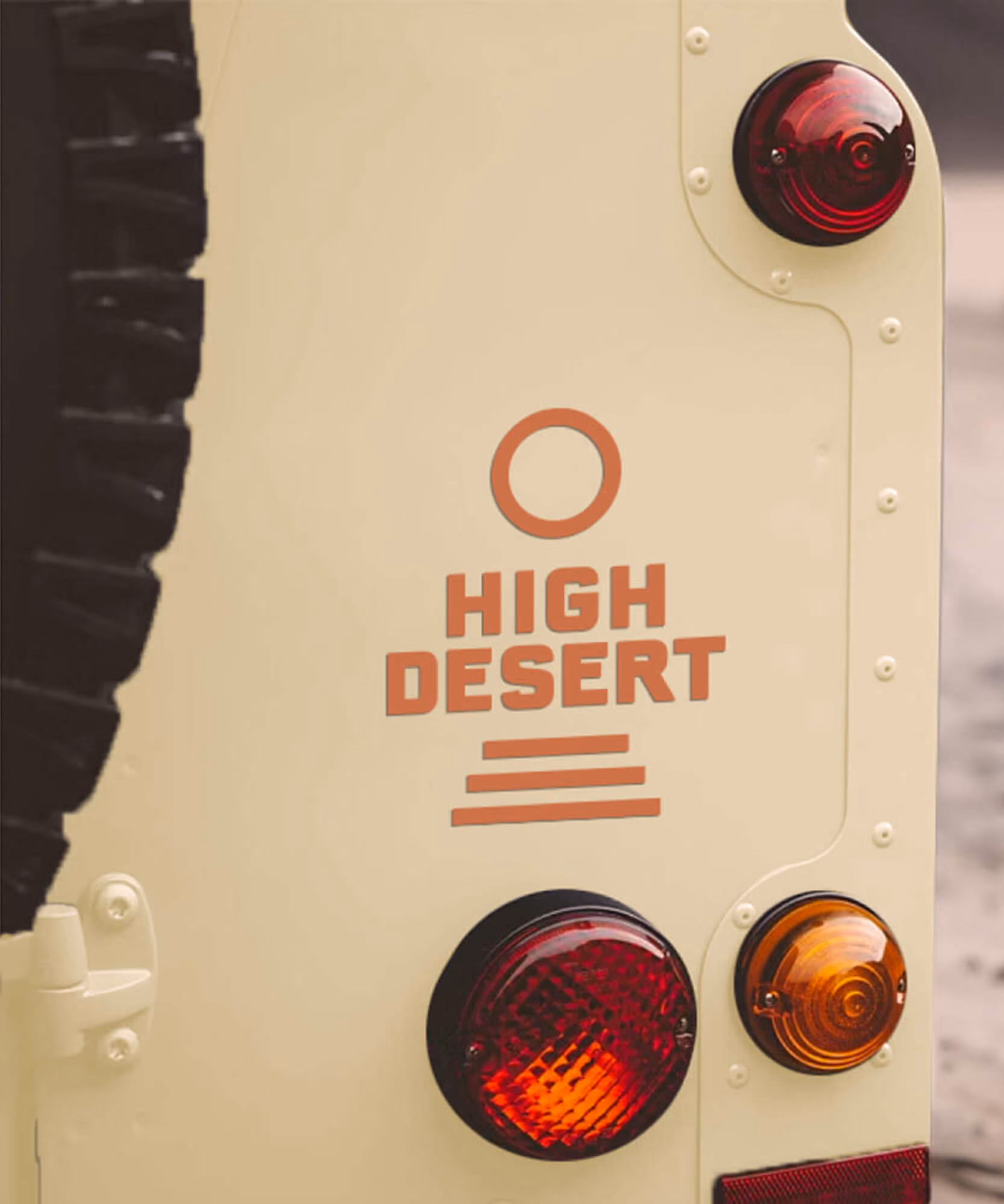 Two orange die-cut stepped 'High Desert' business cards on concrete; cream off-road vehicle with the brandmark behind.