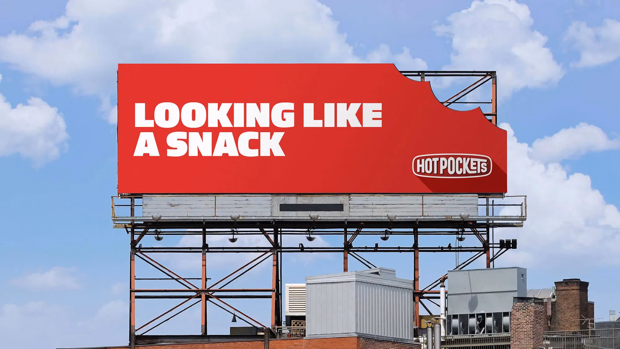 Outdoor billboard against cloudy sky reading 'Looking like a snack' with a bite-corner Hot Pockets logo.