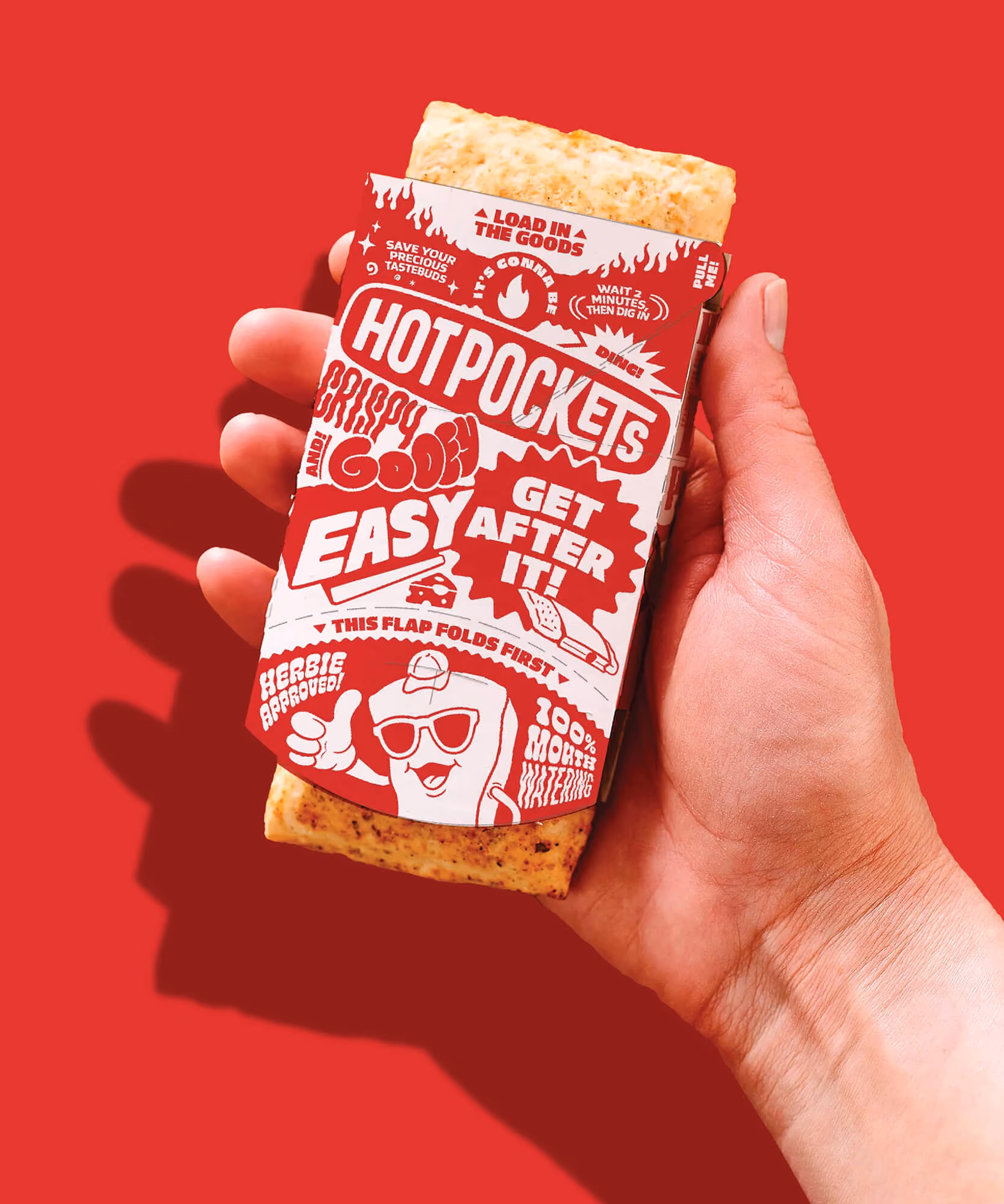 Hand holding a Hot Pocket in a red sticker-print sleeve with 'Load it,' 'Heat it,' 'Enjoy it' and a cartoon mascot.