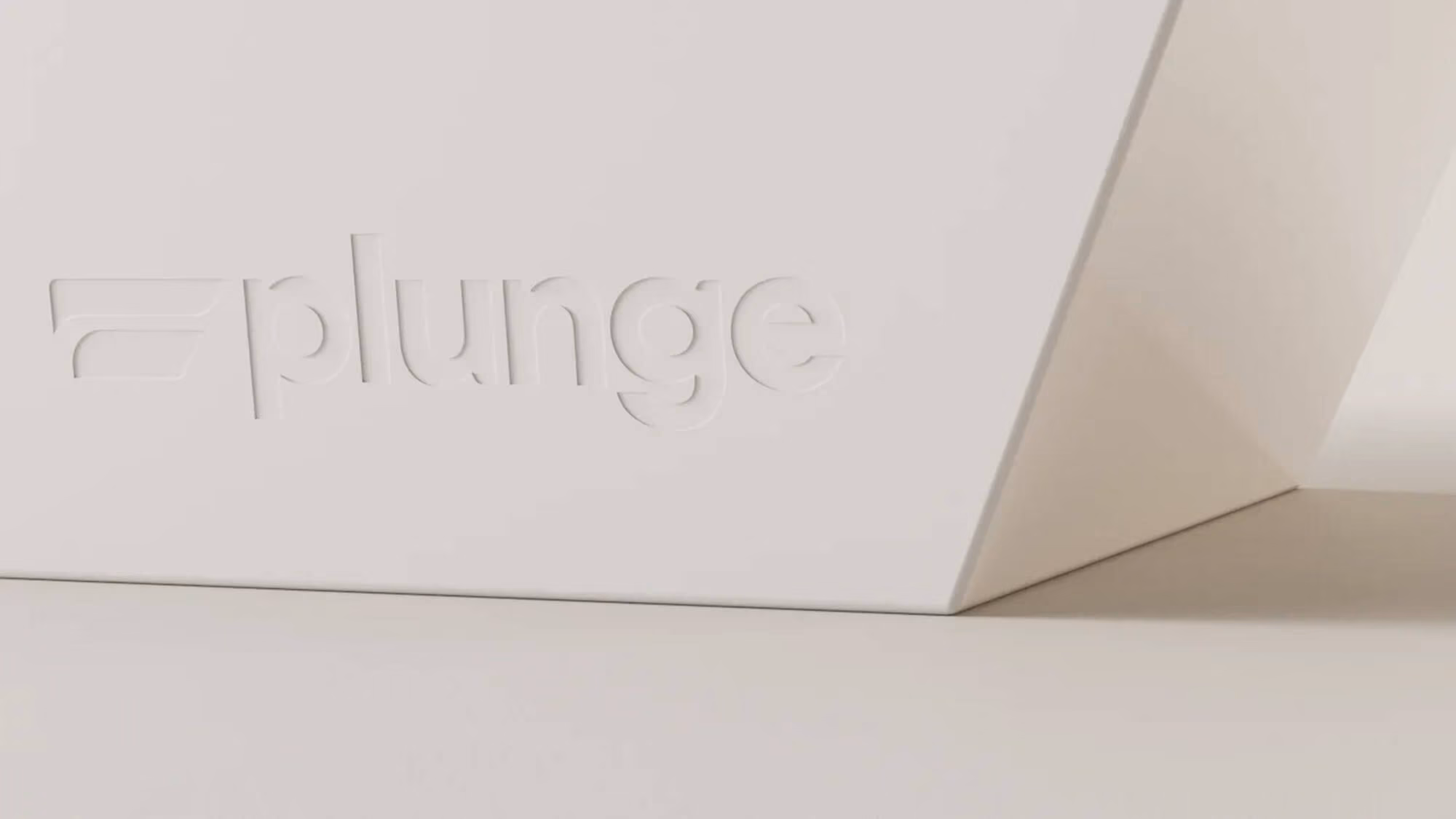 Close-up of a white Plunge tub corner with the wordmark debossed into its angled side panel.