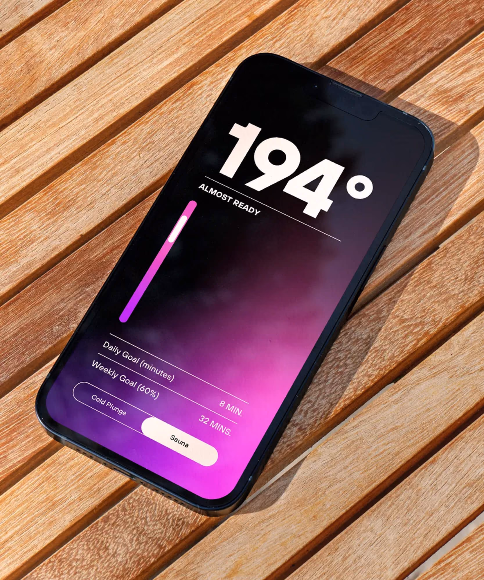 Smartphone on slatted wood decking with a pink-purple gradient sauna timer screen reading '194 degrees, almost ready'.