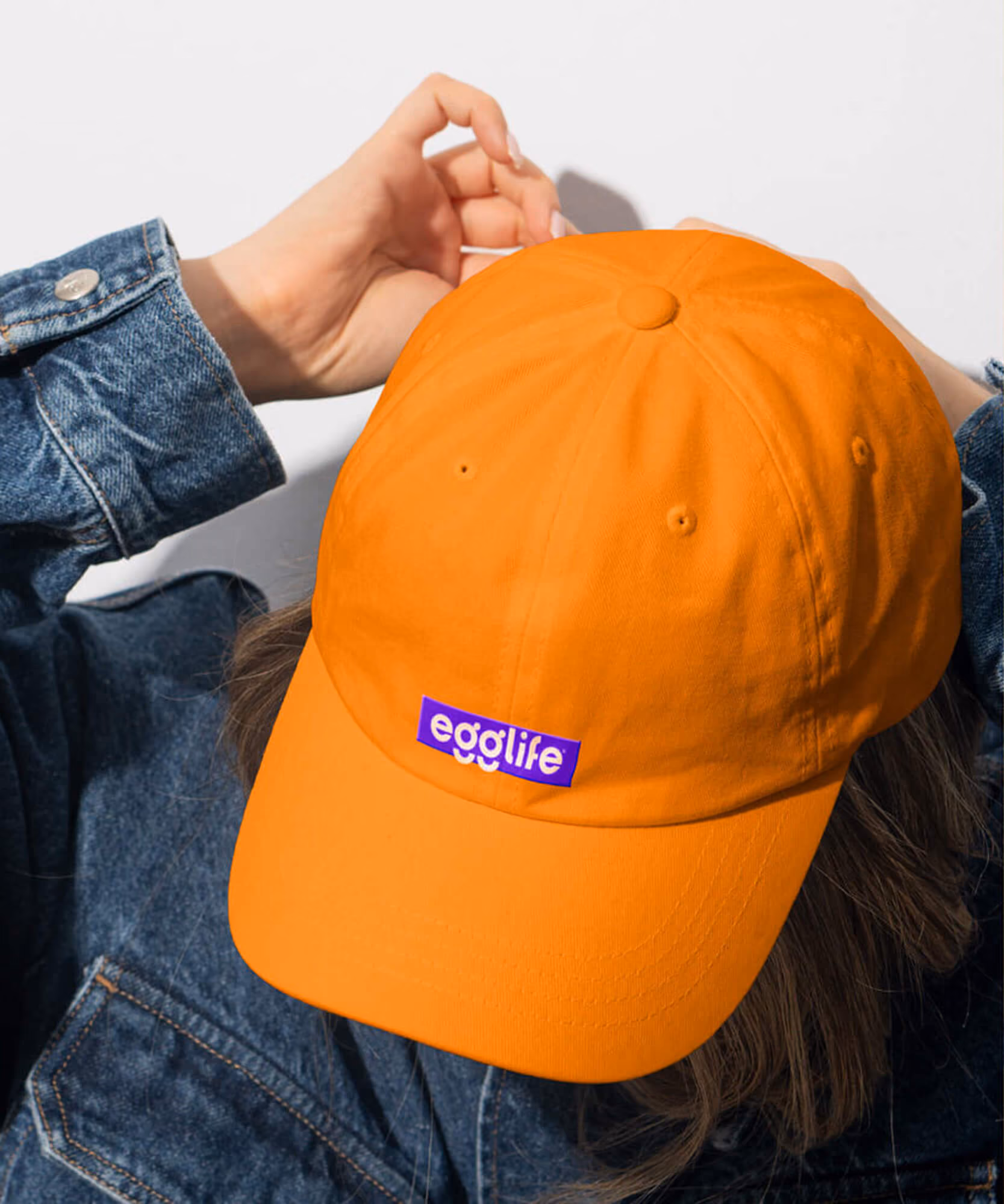 Person wearing an orange cap with a purple label reading 'egglife' and a denim jacket.