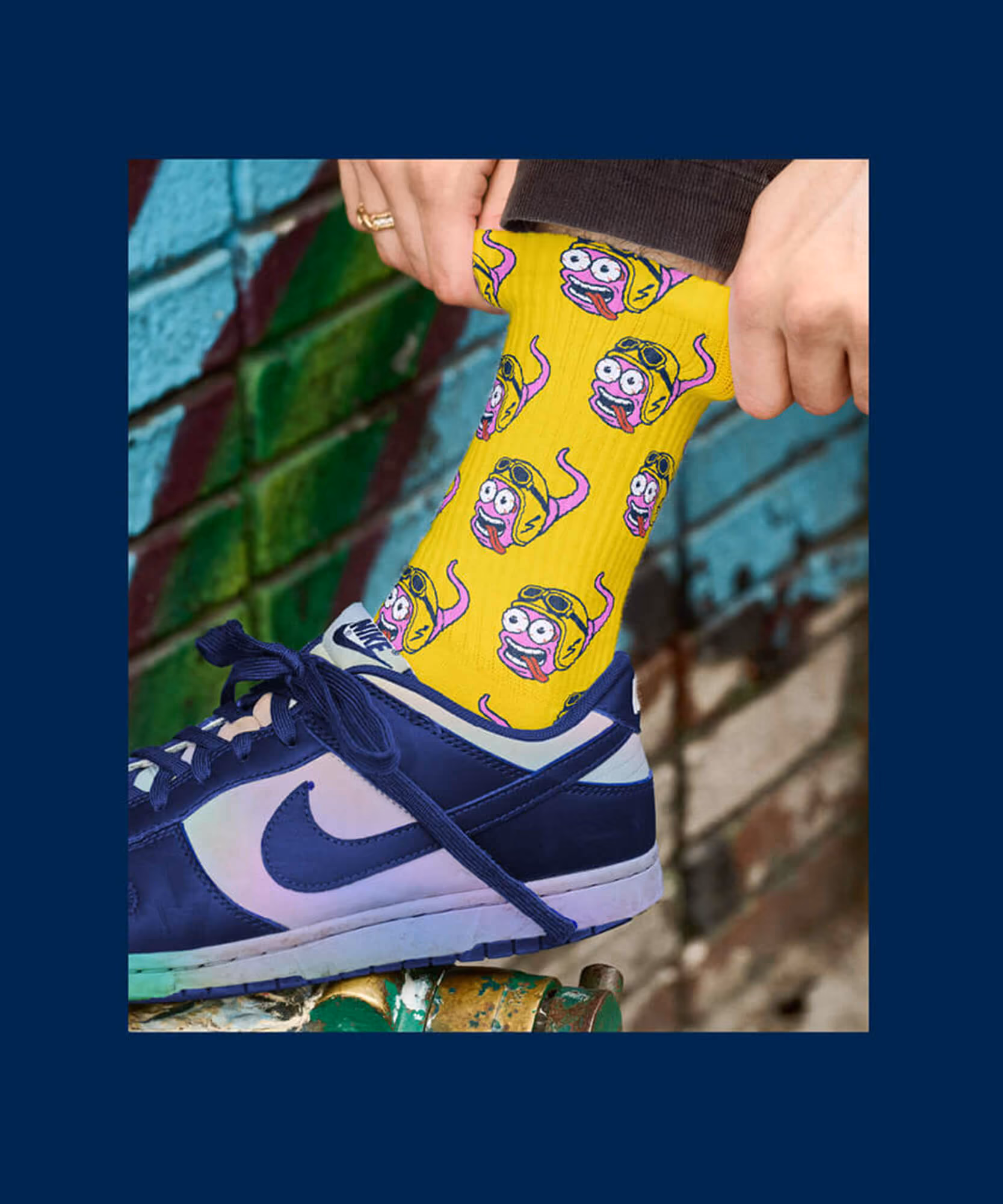Person adjusting bright yellow Sperm Worms socks with cartoon faces wearing aviator helmets and goggles above a navy and white shoe.