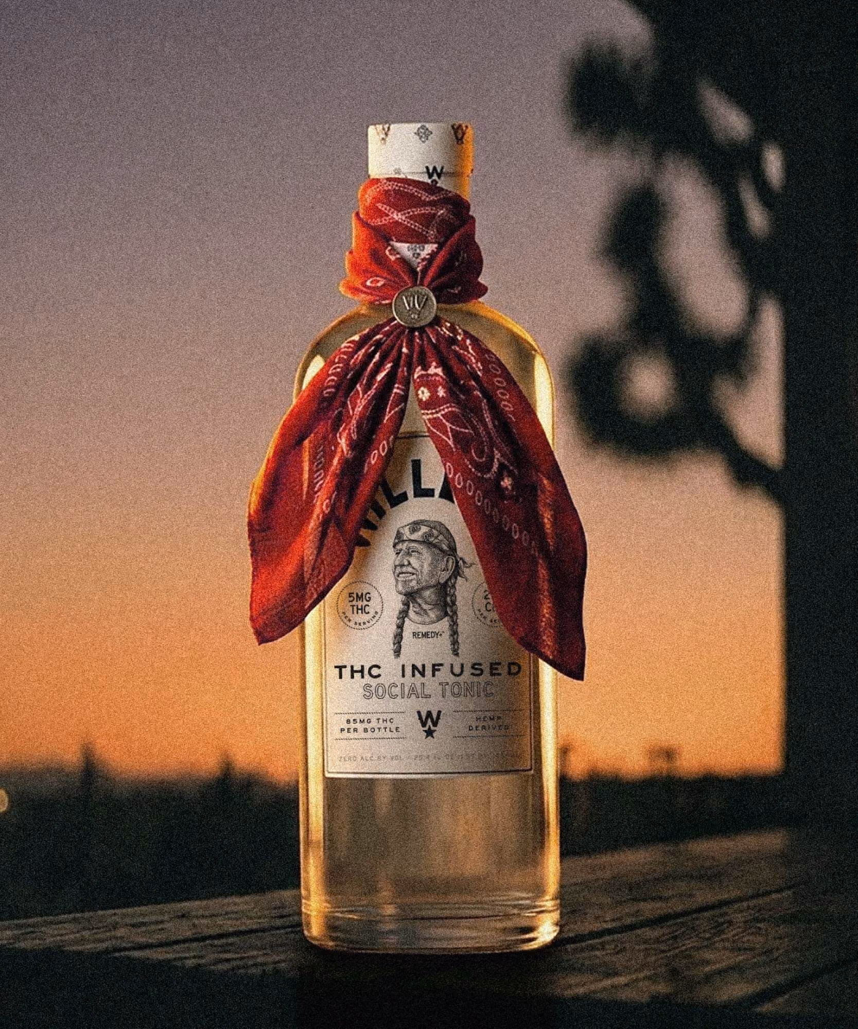 Willie's "THC Infused Social Tonic" bottle with a red paisley bandana tied at the neck at sunset