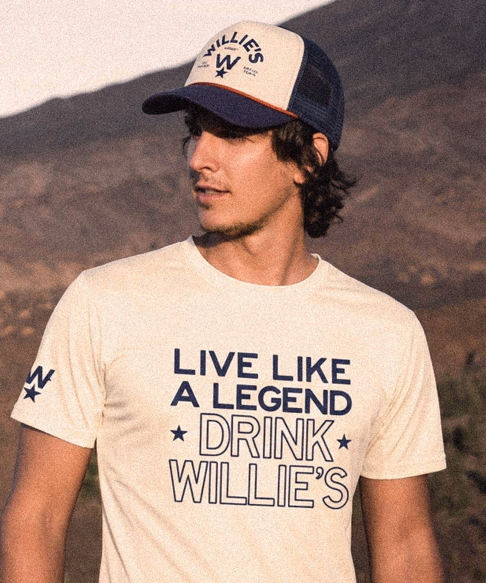 Man in a cream tee reading "Live like a legend, drink Willie's" and a navy trucker cap