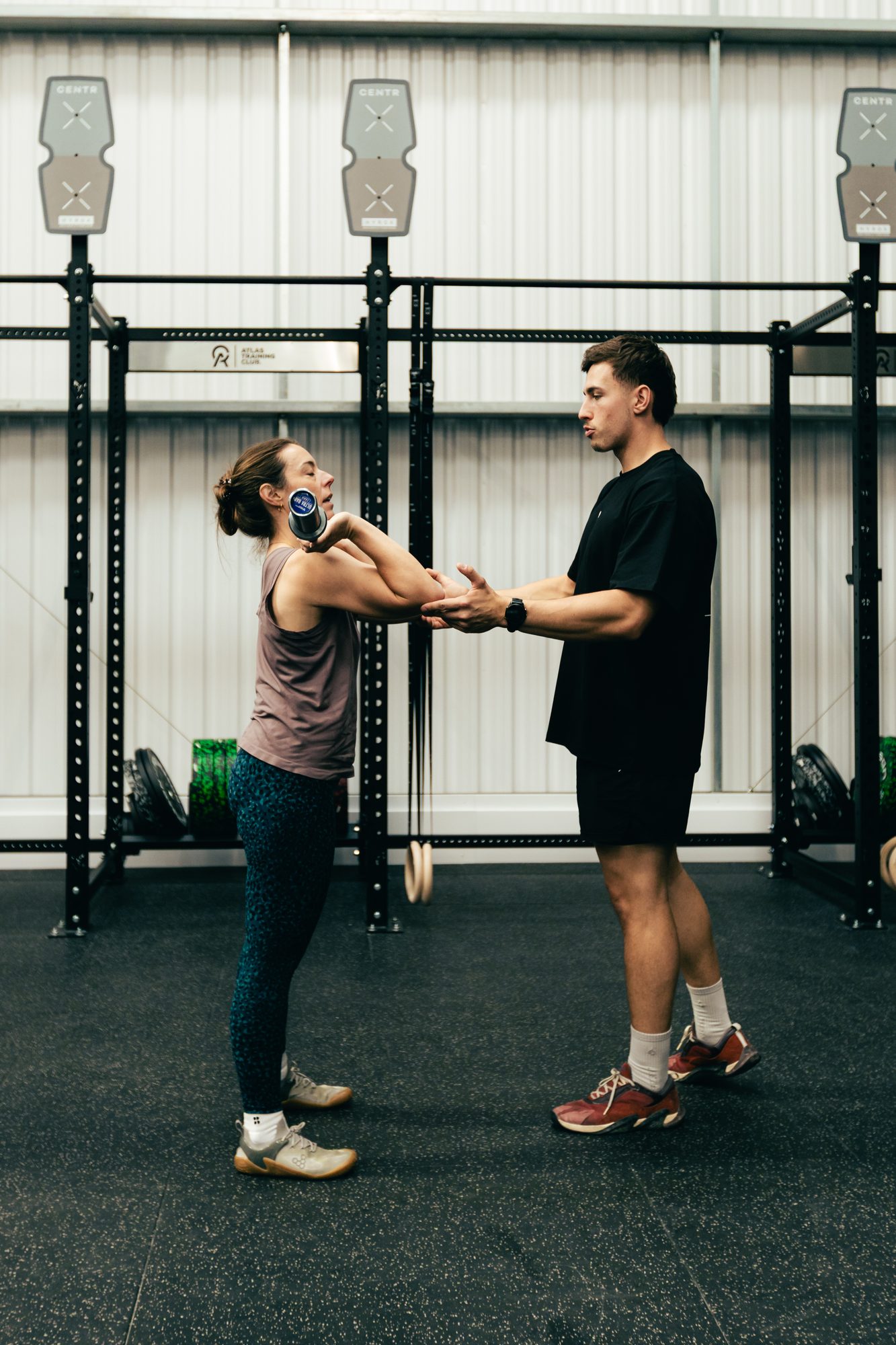 Personal training session at Atlas Training Club — coach cueing a member's form on the gym floor
