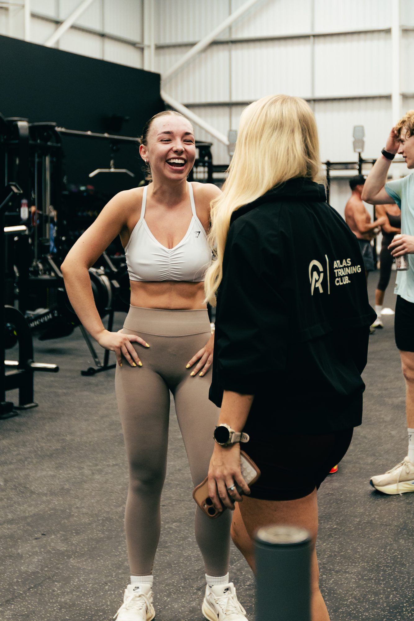 An Atlas Training Club coach in branded kit talking with a member on the gym floor