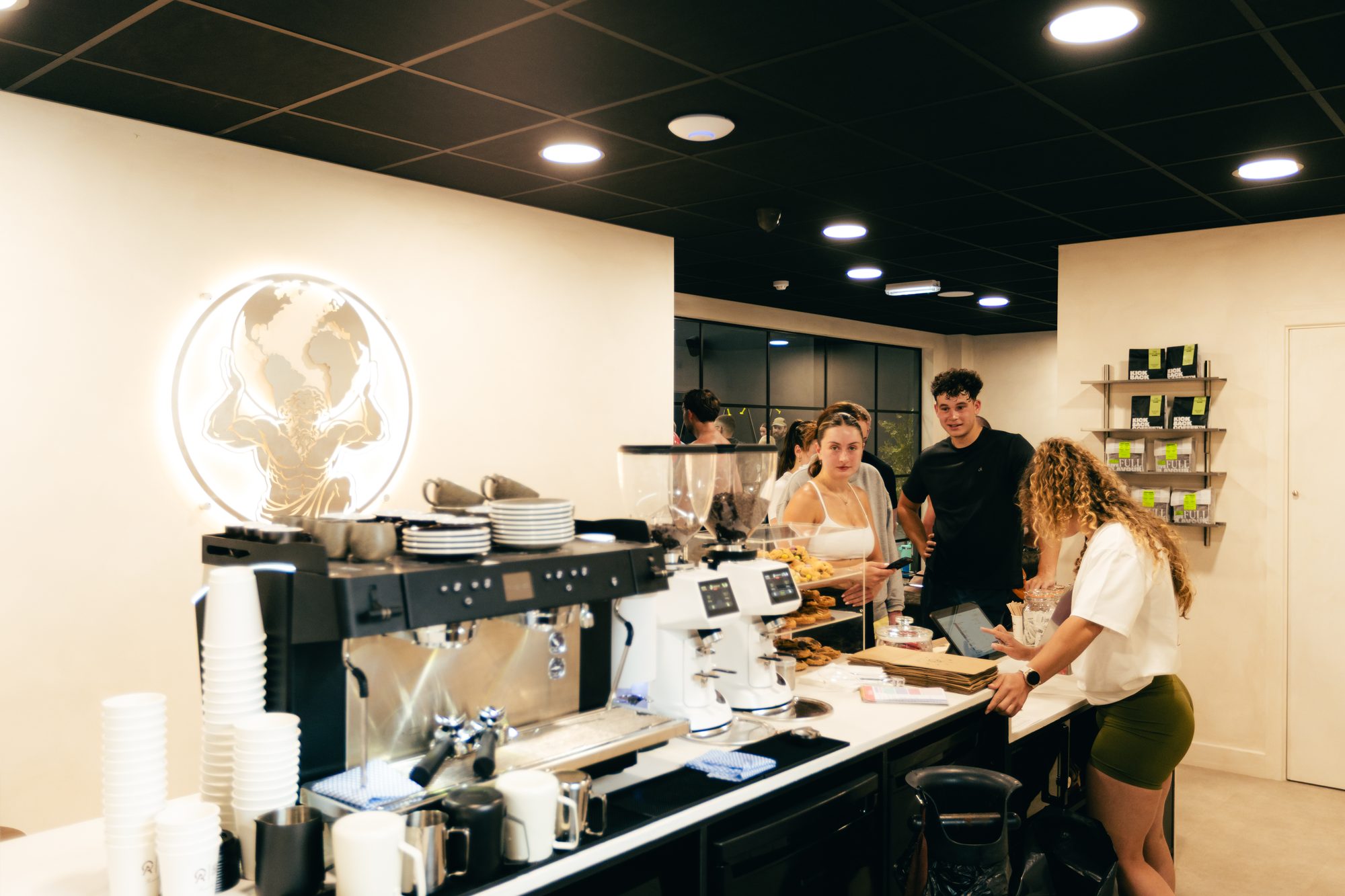 The café counter at Atlas Training Club — coffee, fresh pastries and members ordering under the illuminated Atlas logo