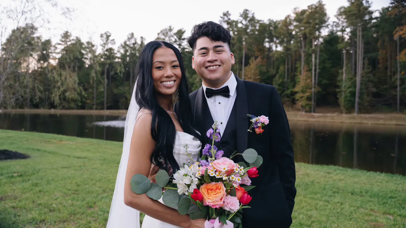 Bride with long straight hairstyle and veil holding a colorful bouquet at a lakeside wedding venue, styled by Dayln Faith Hair and Beauty