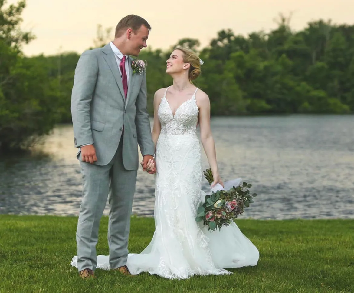 Bride with elegant updo and floral hair accent at a lakeside wedding at sunset, styled by Dayln Faith Hair and Beauty
