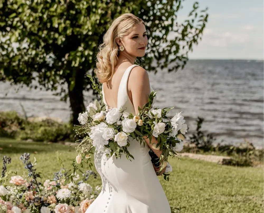 Blonde bride with soft romantic waves holding a white floral bouquet at a waterfront wedding venue in North Carolina