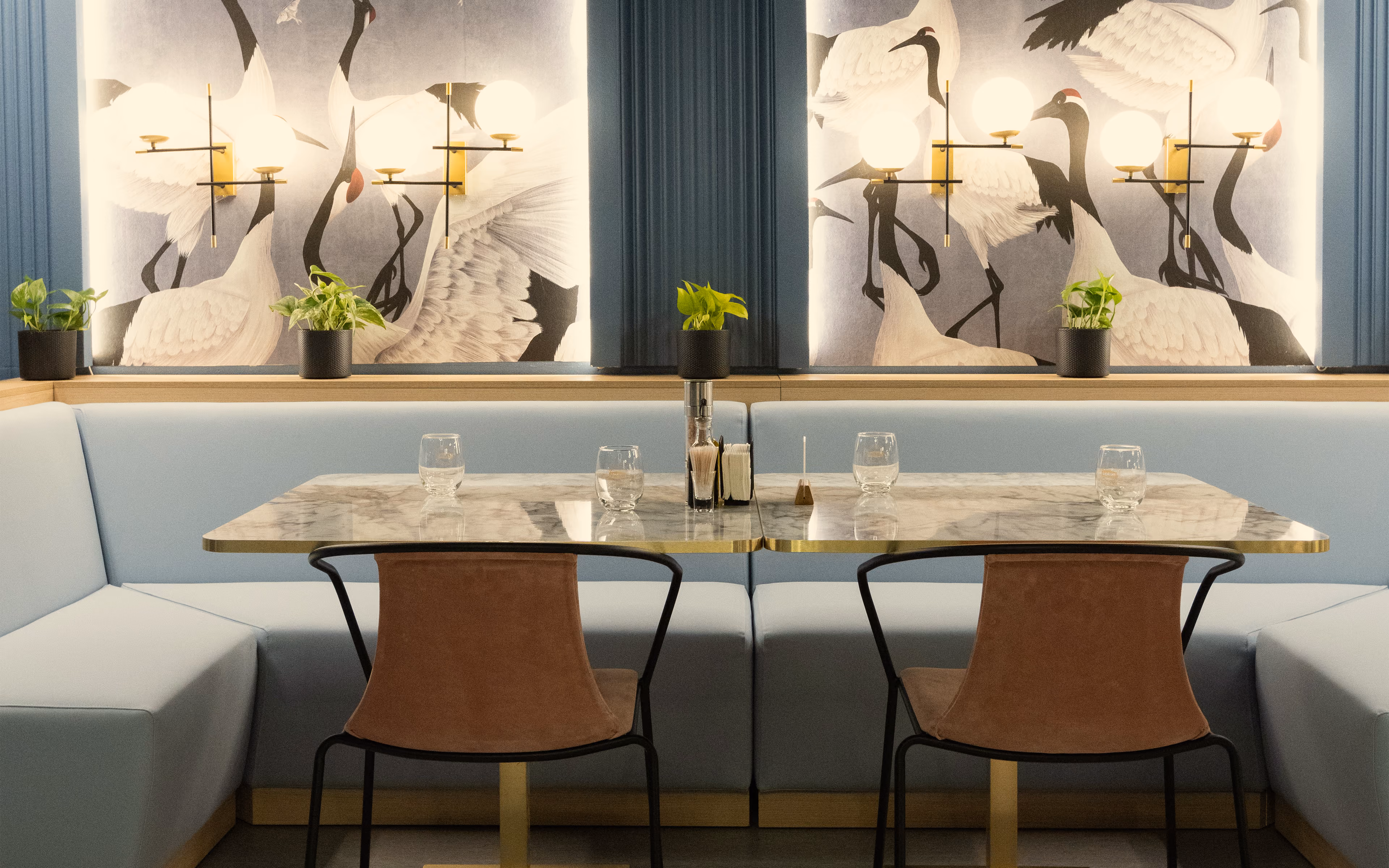 Modern restaurant seating with marble tables, brown chairs, light blue bench, and crane bird wall art.