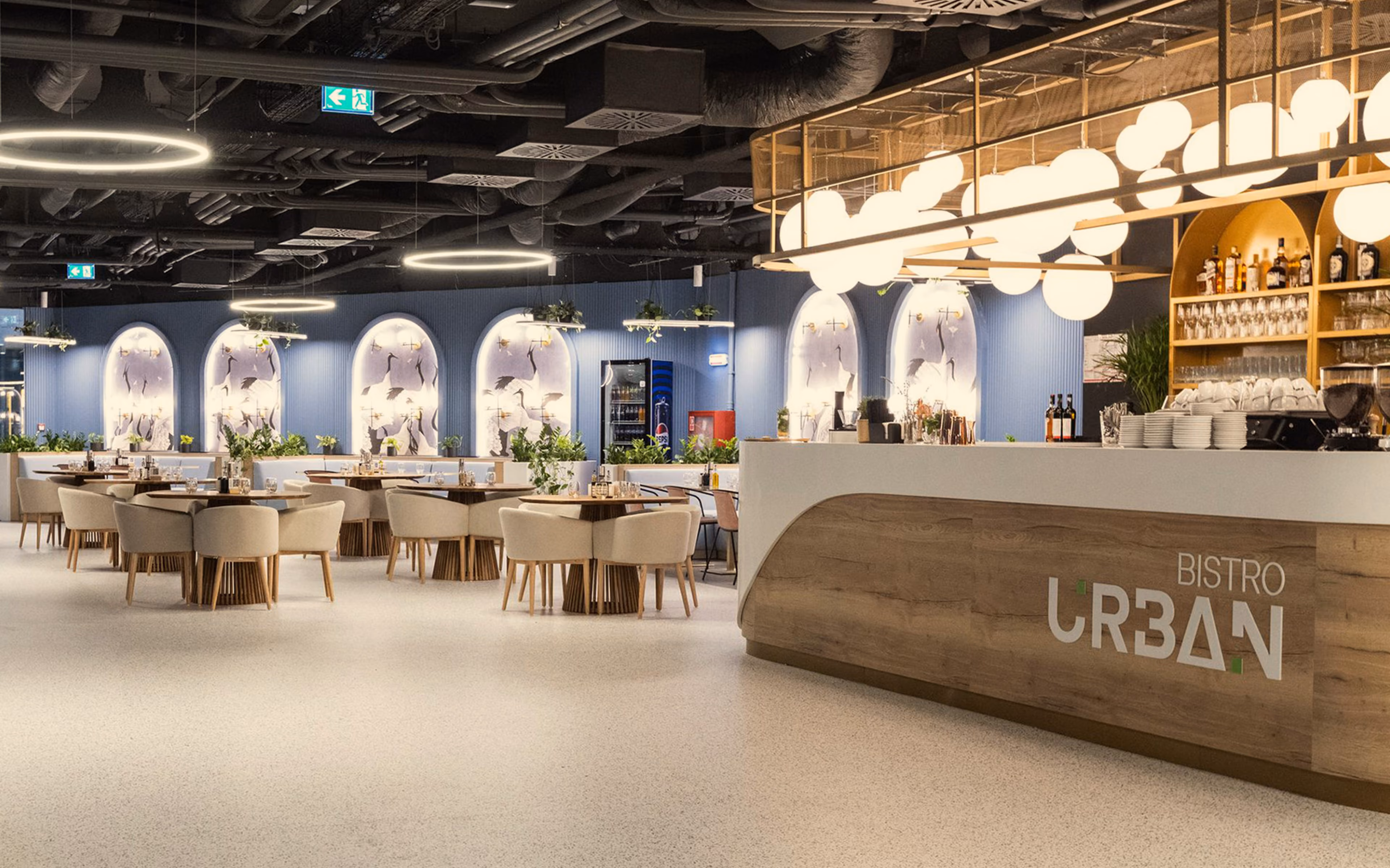 Modern bistro interior with wooden tables, beige chairs, blue walls, and illuminated bar counter.