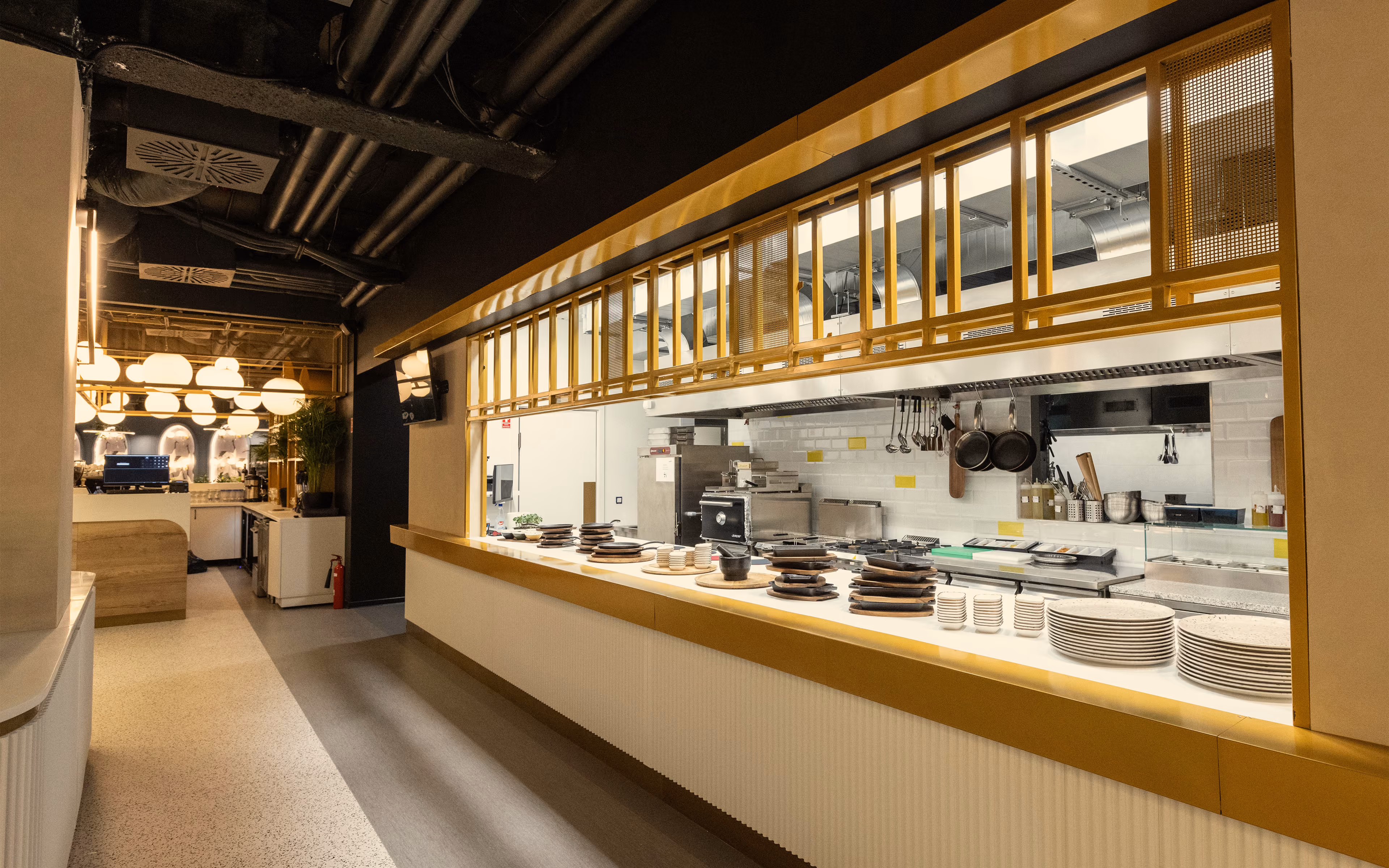 Modern restaurant open kitchen with rows of stacked plates and cooking utensils on counter.