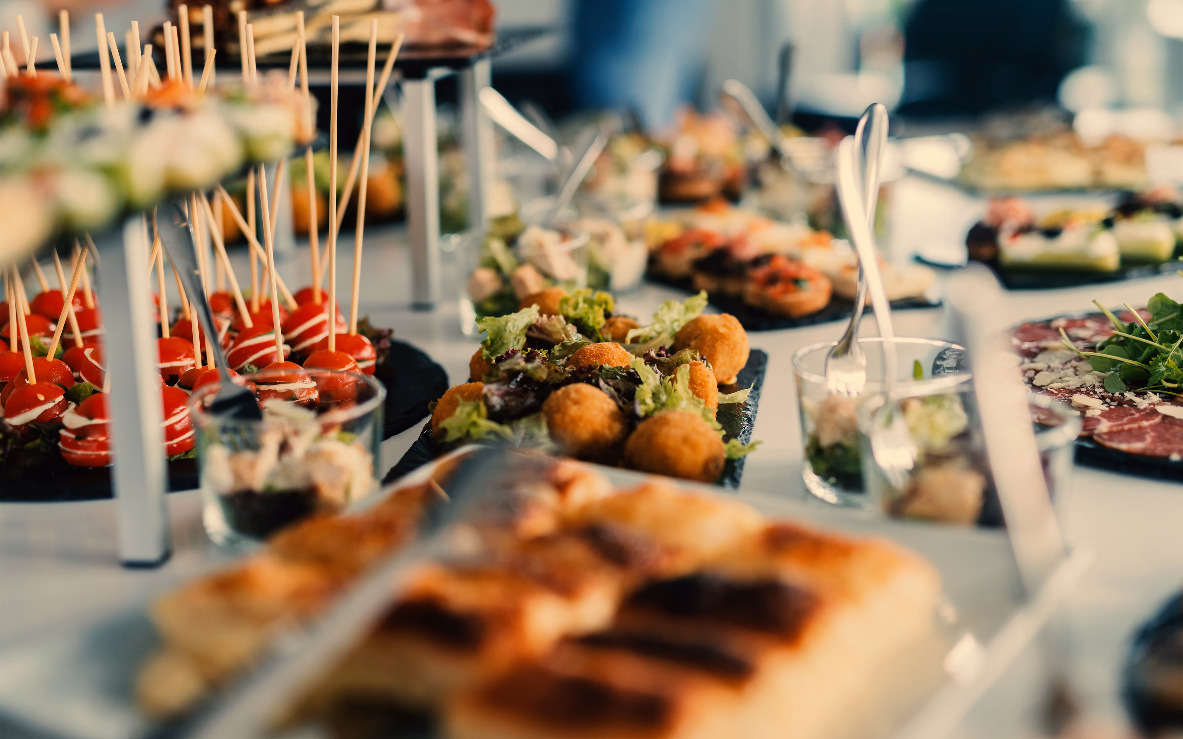 Buffet table with various appetizers including tomato skewers, salad, and fried croquettes.