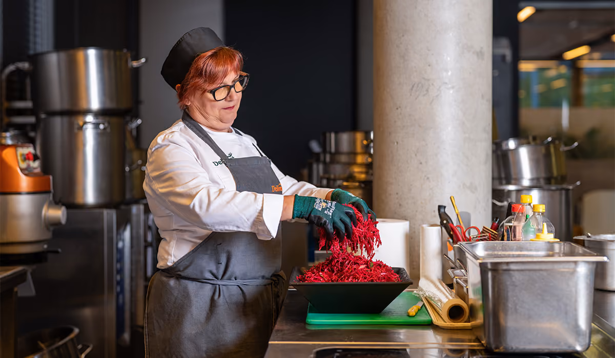 Chef wearing glasses and gloves preparing shredded red cabbage in a professional kitchen.
