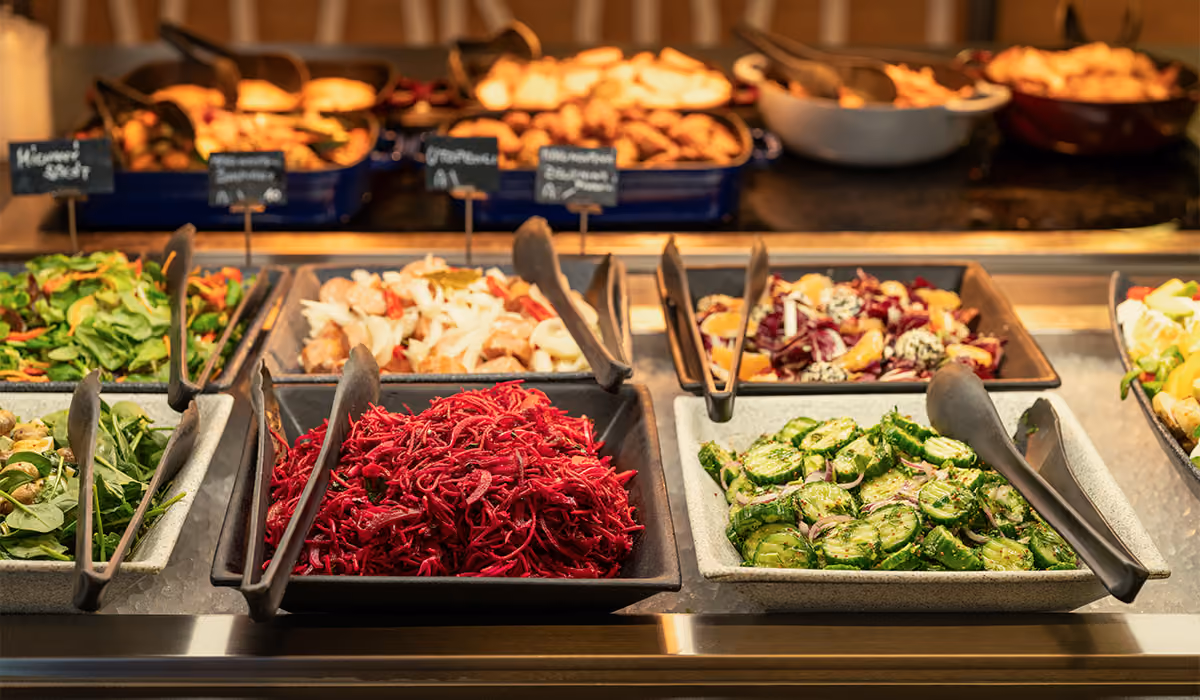 Buffet salad bar with various fresh salads including shredded beets and cucumber salad in square bowls.