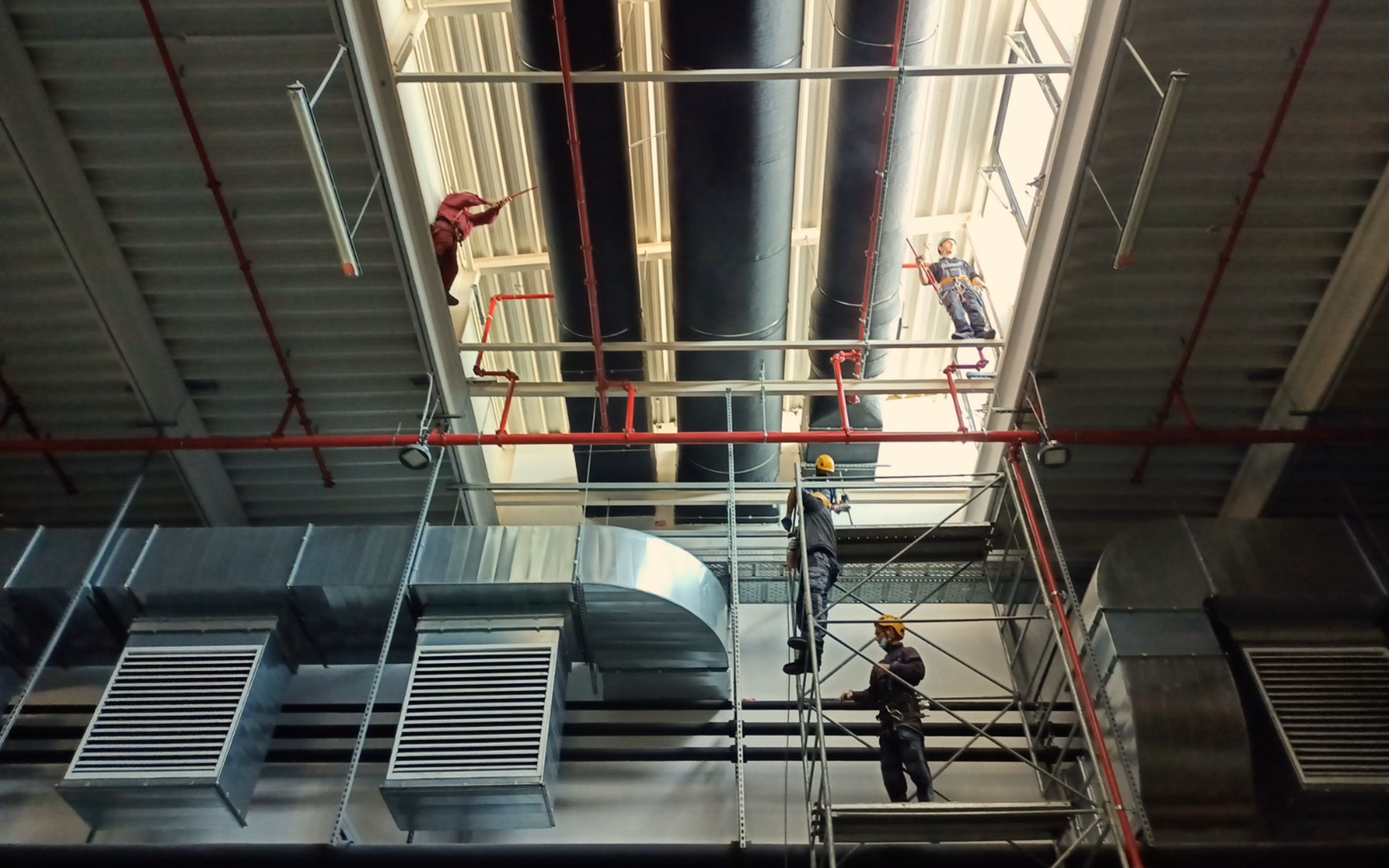 Workers on scaffolding and ceiling repairs inside a large industrial ventilation system area.