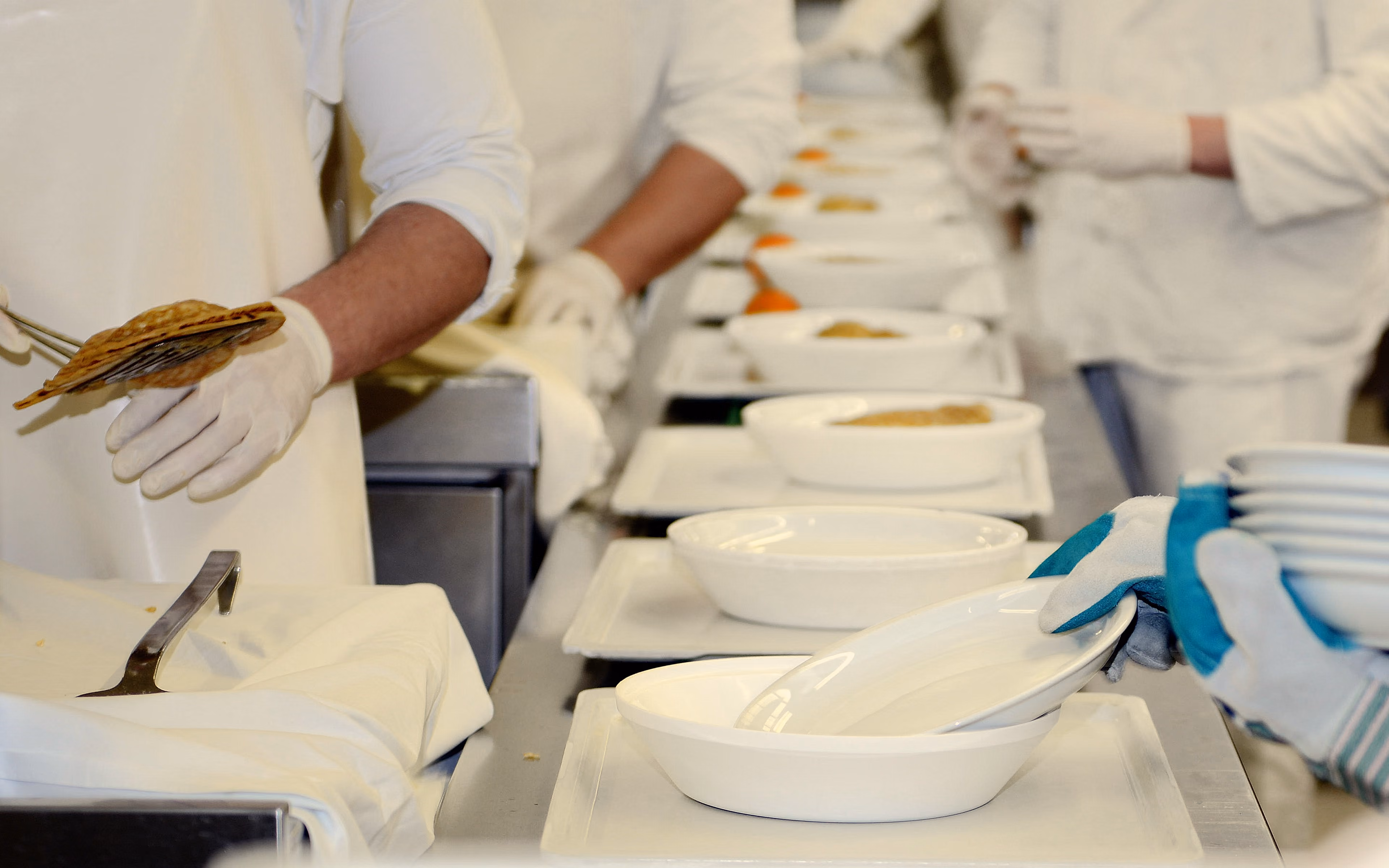 Food service staff in white uniforms preparing and arranging dishes on a serving line.