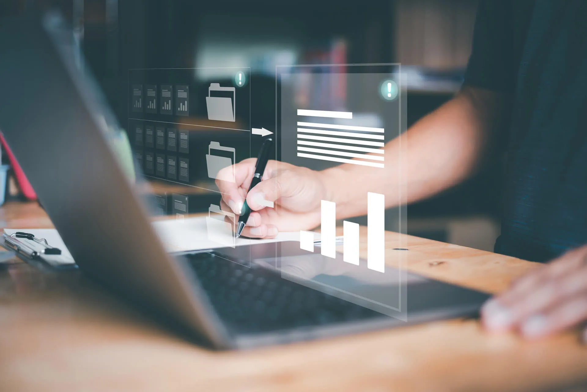 Person writing with pen on paper beside laptop with digital folder and charts overlay.
