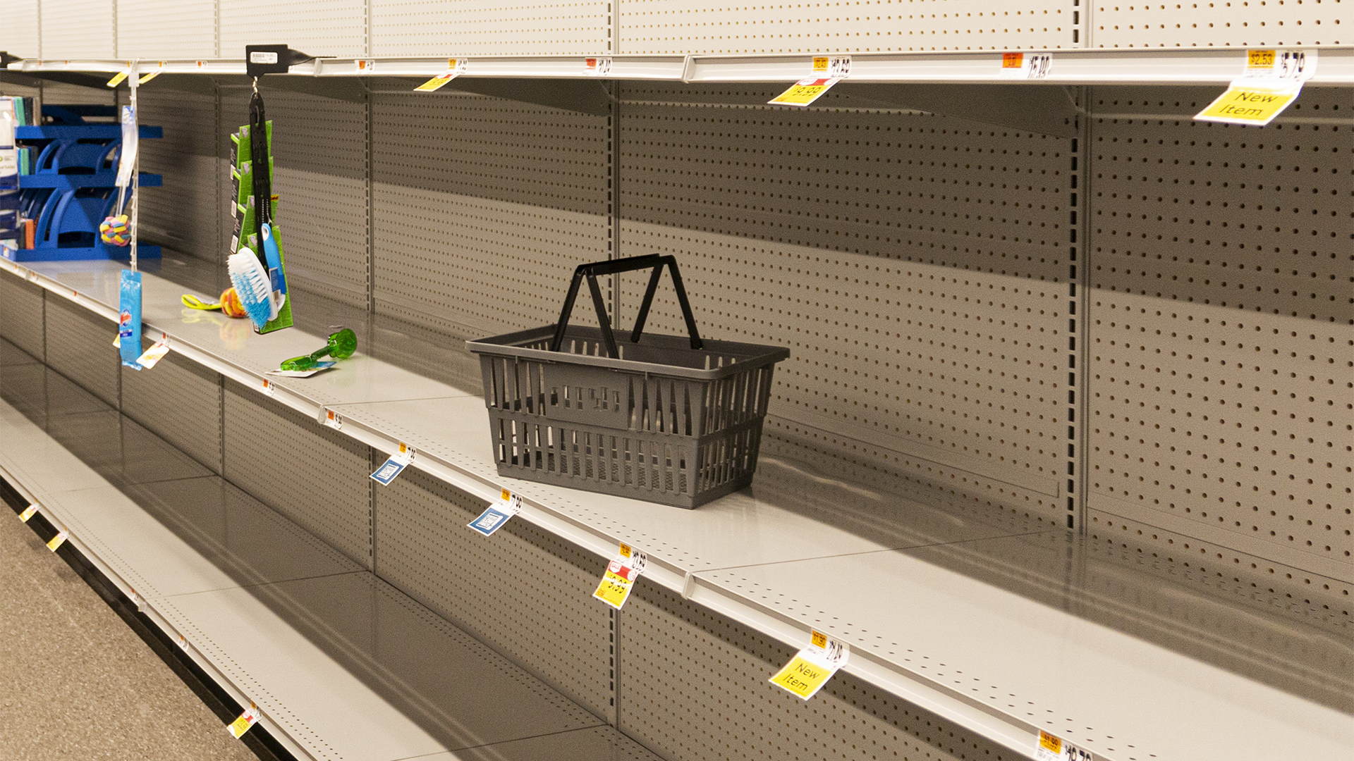 Empty grocery store shelves with a single black shopping basket left behind