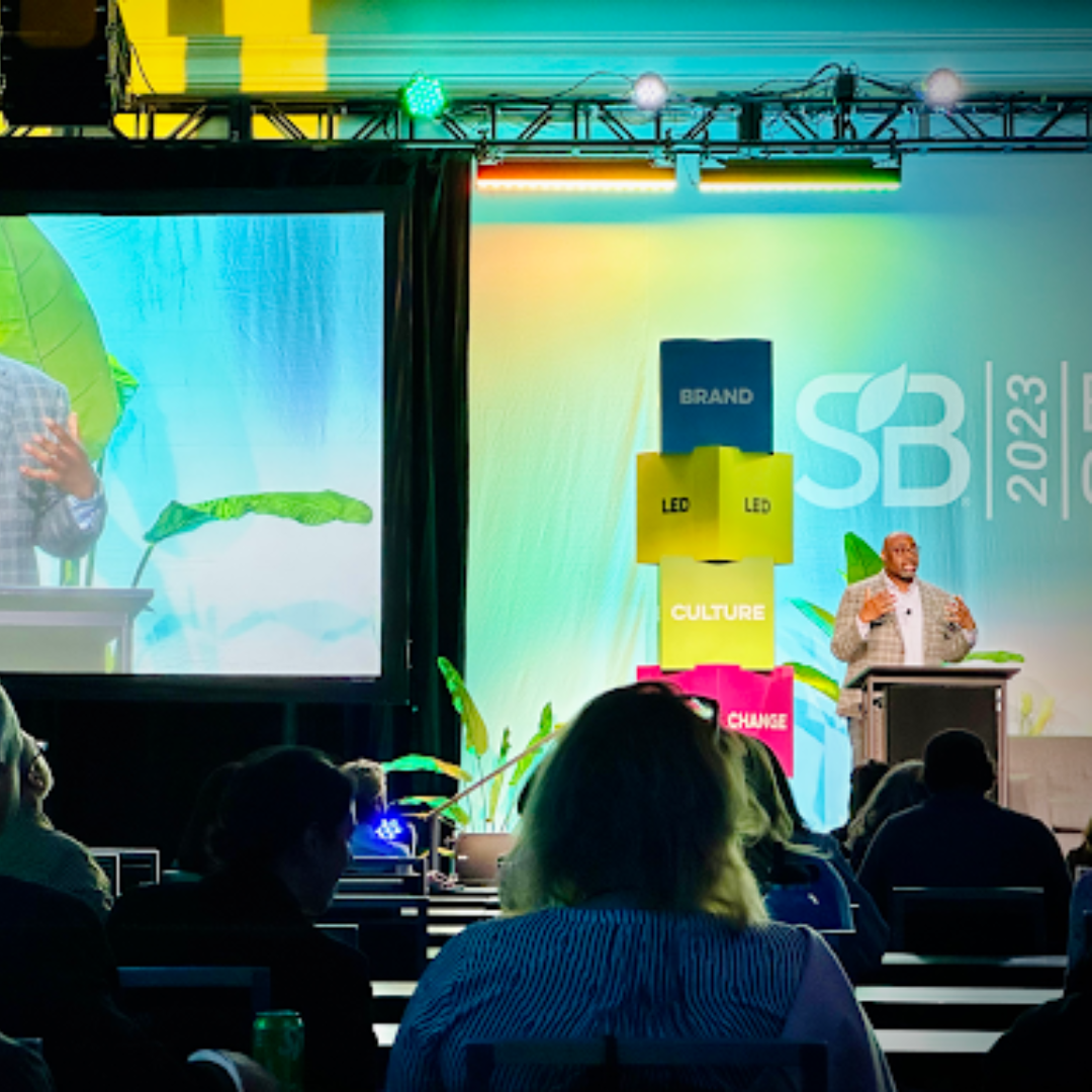 Samuel Monnie speaking at a podium beside the stacked SB 2023 Brand Led Culture Change stage set