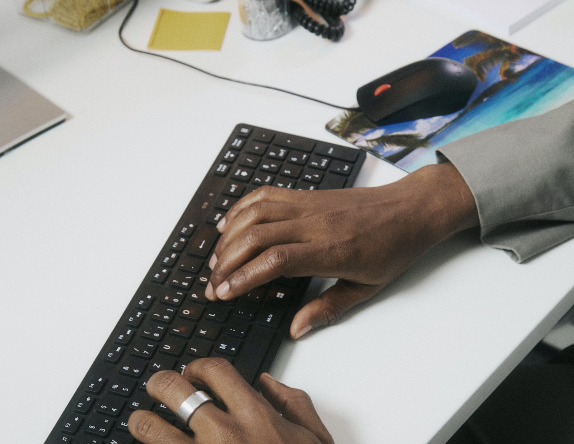 Hands typing on a keyboard at a white desk beside a tropical mouse pad