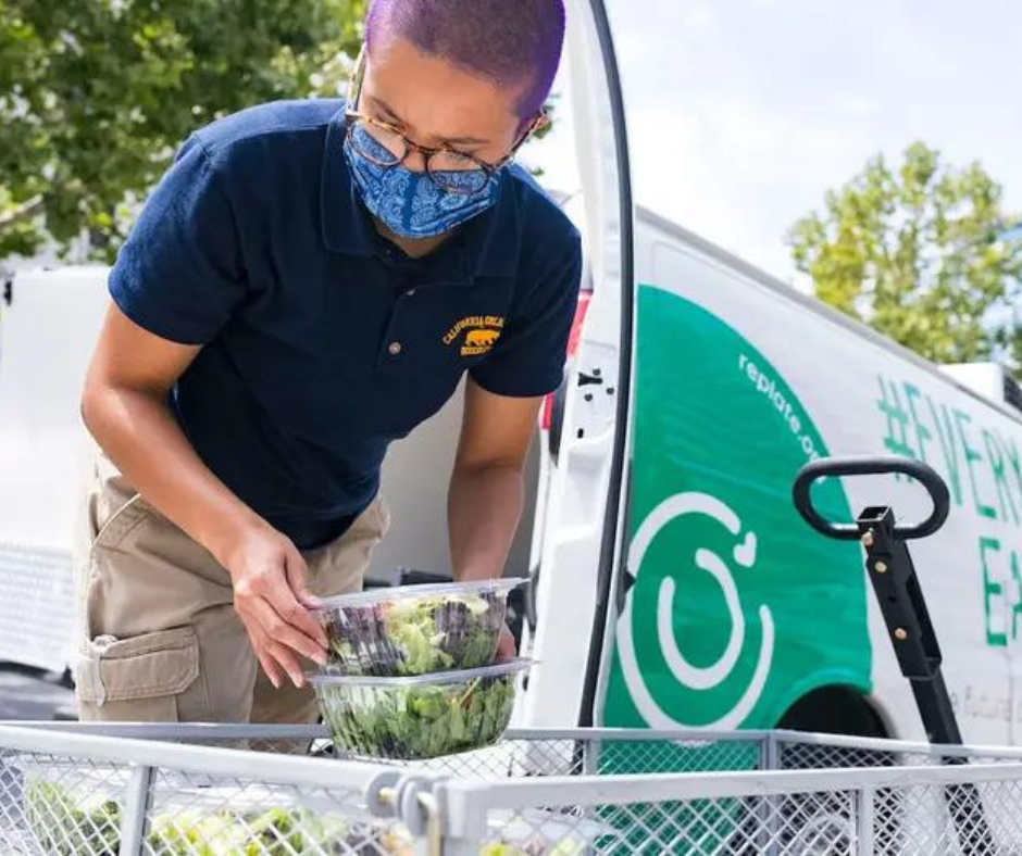 Replate volunteer loading trays of salad into a van