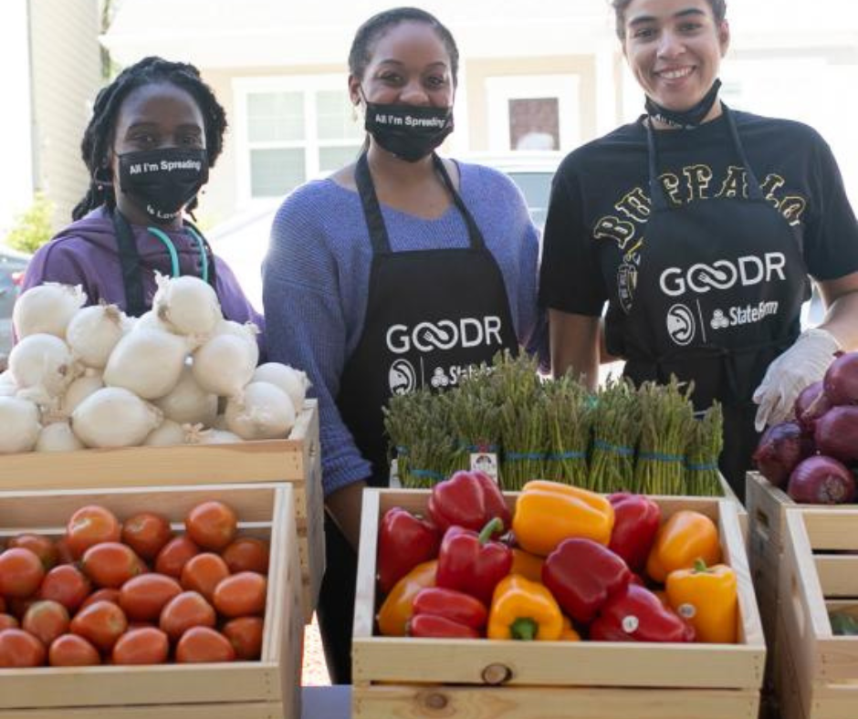 Goodr volunteers in aprons behind crates of tomatoes, peppers, onions and asparagus