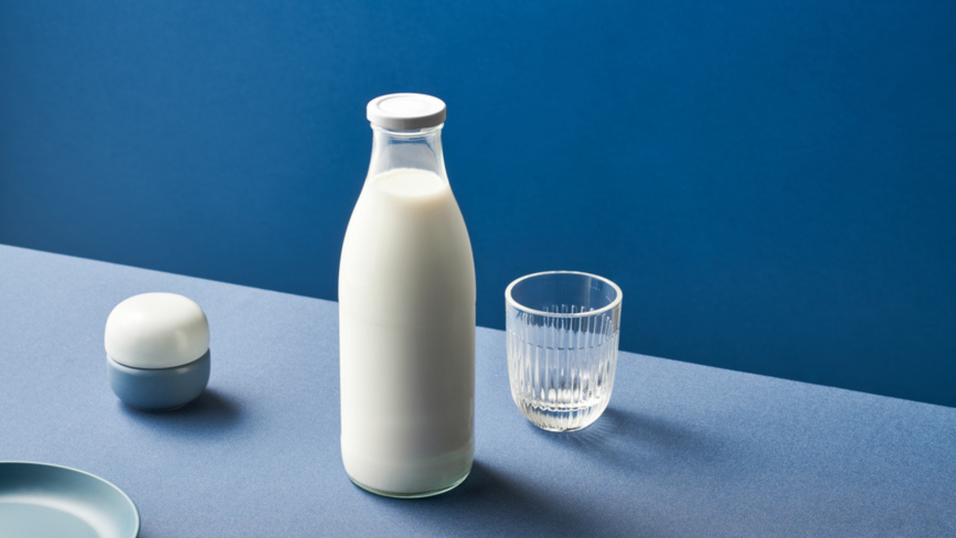 Bottle of milk and an empty ribbed glass on a blue table