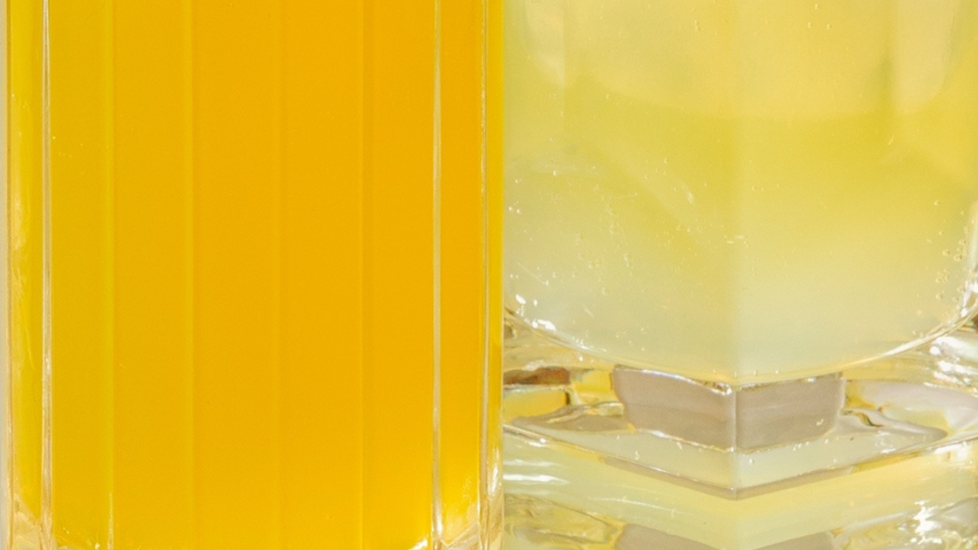Close-up of a glass of orange juice next to a glass of pale lemonade