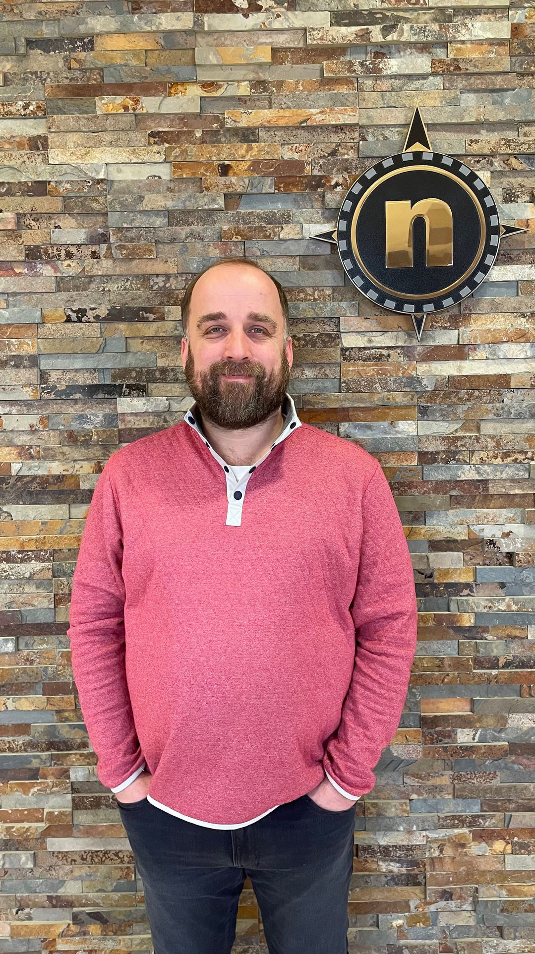 John Herbert standing in front of a stone wall with the True North compass logo