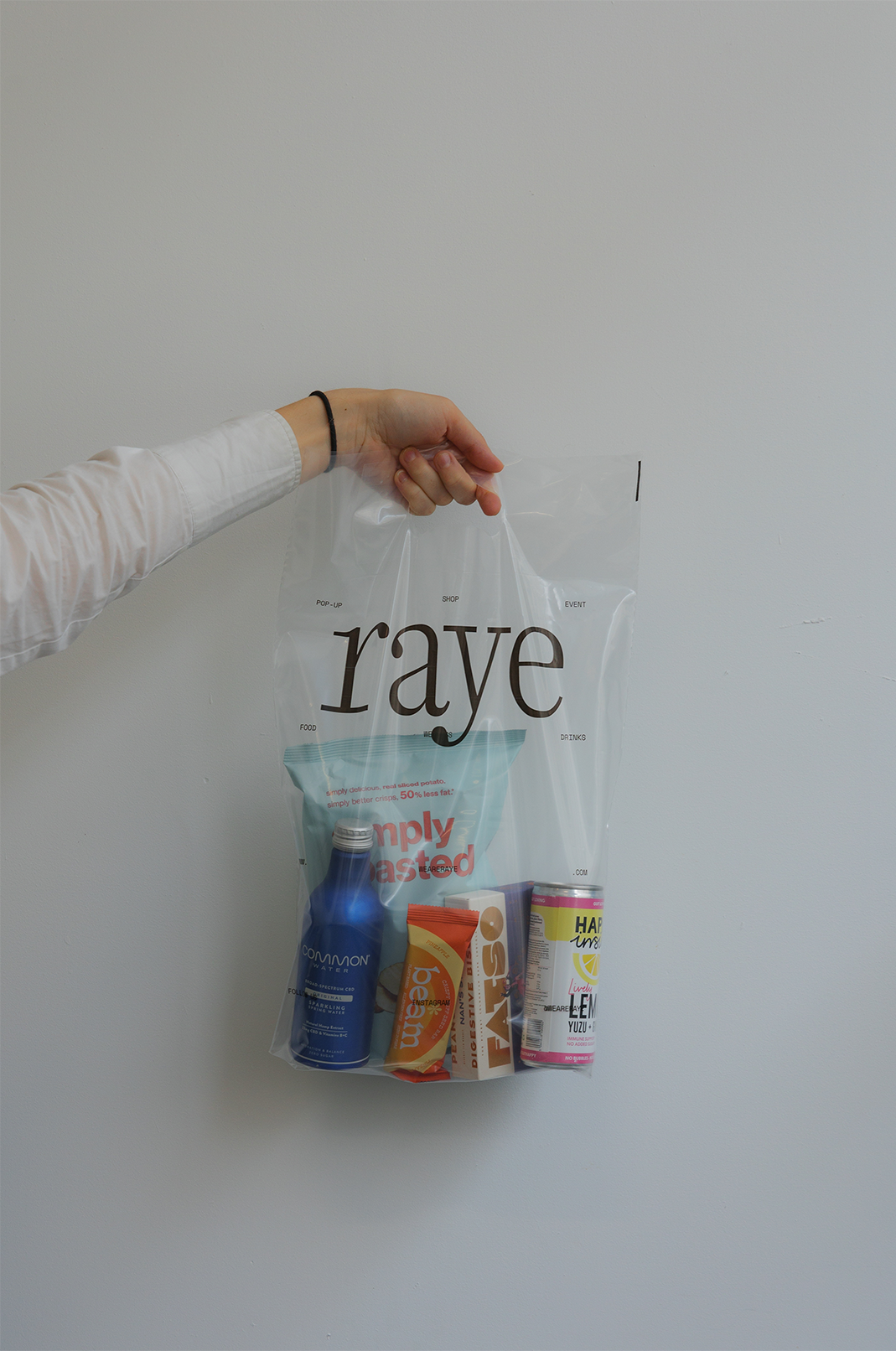 Hand holding a clear Raye checkout bag filled with drinks and snacks