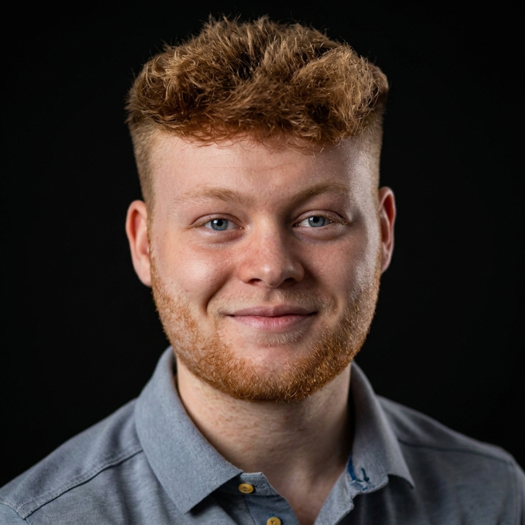 Portrait of a young man with curly red hair and beard, smiling slightly, wearing a gray collared shirt against a black background.