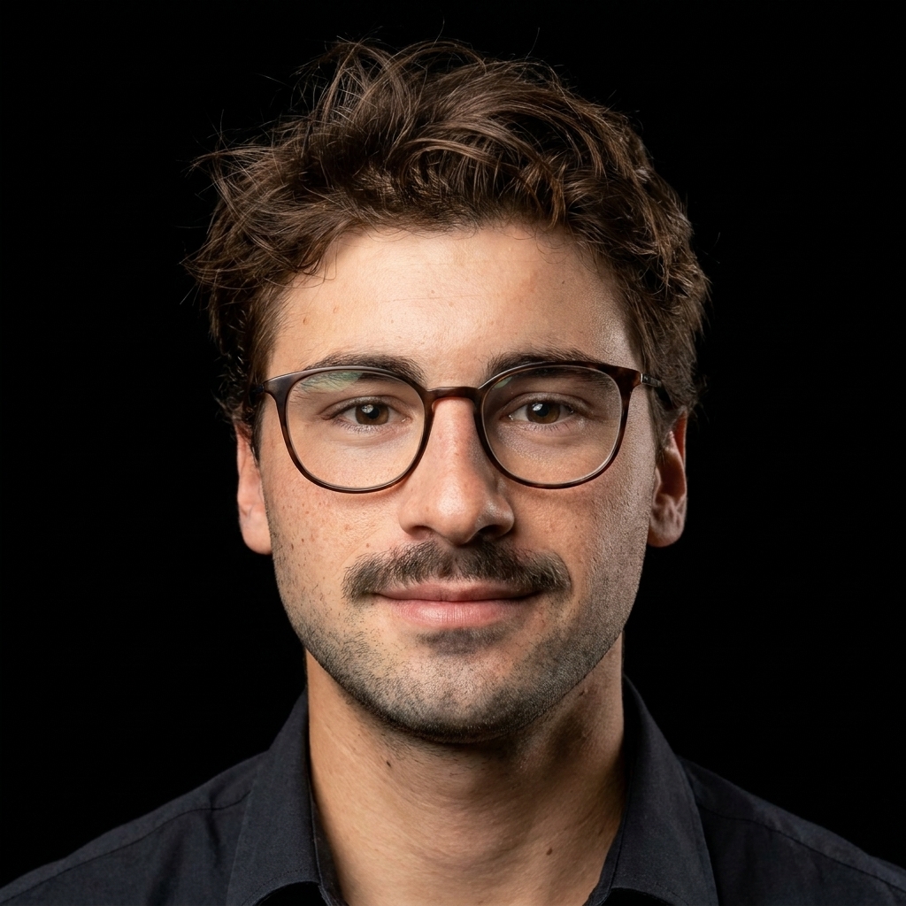 Young man with glasses and a mustache wearing a black shirt against a black background.