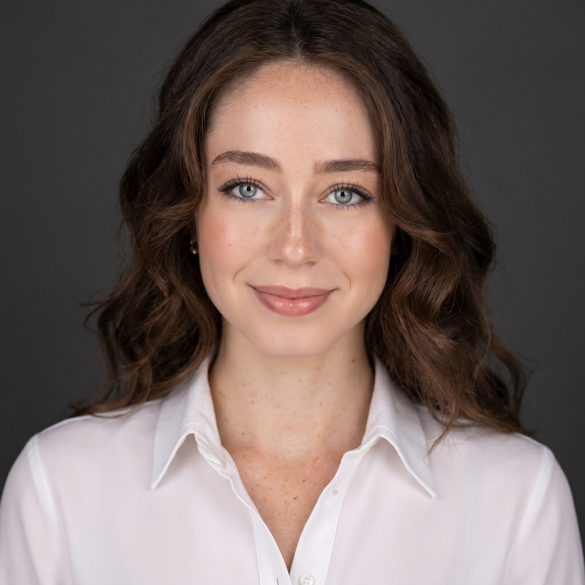 Portrait of a woman with wavy brown hair, blue eyes, wearing a white button-up shirt against a black background.