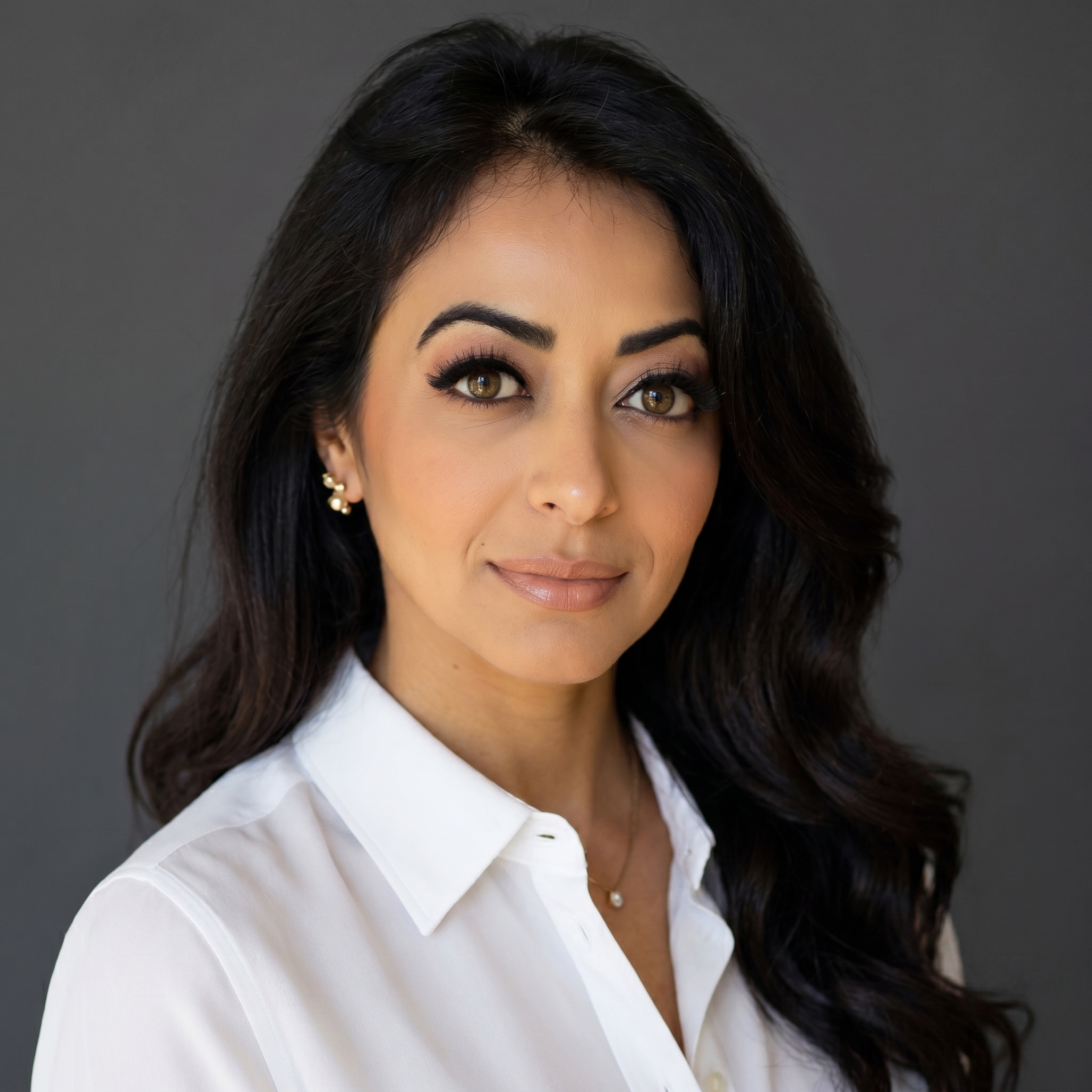 Portrait of a woman with dark hair wearing a white collared shirt and gold earrings against a black background.