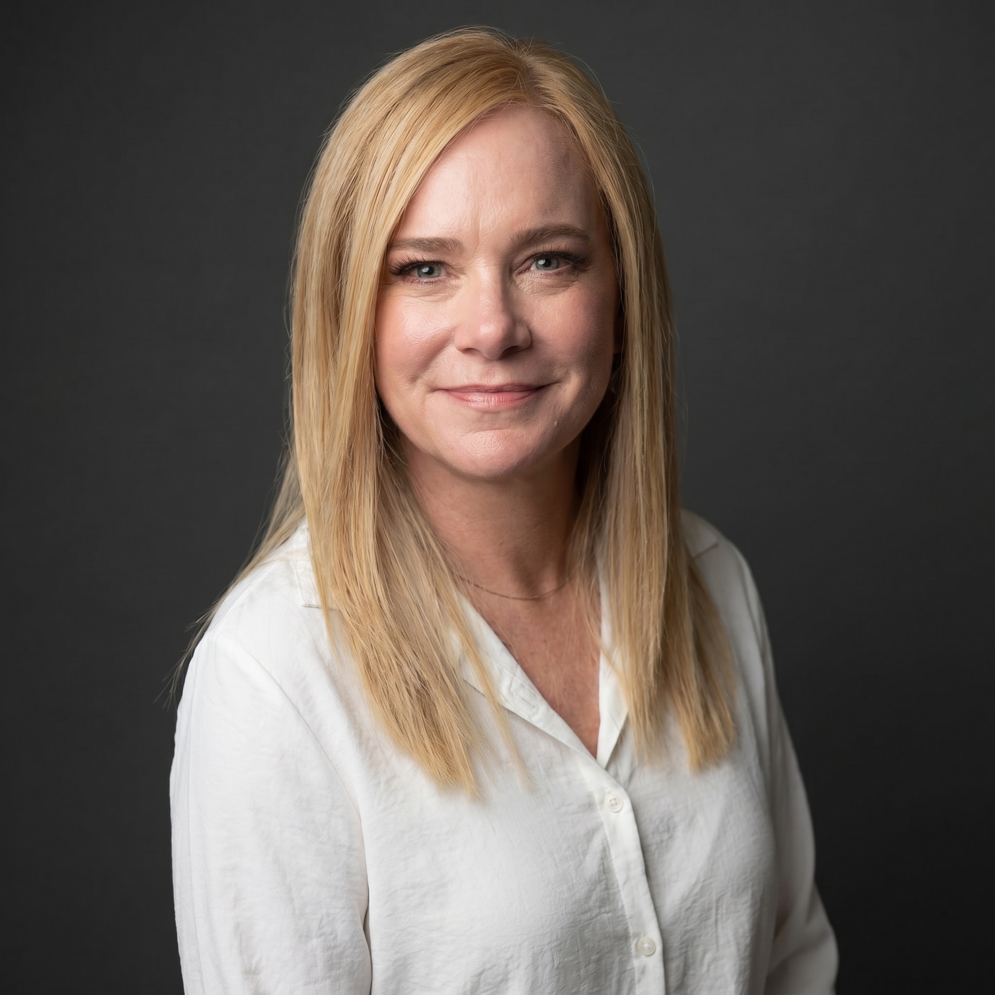 Portrait of a woman with wavy brown hair, blue eyes, wearing a white button-up shirt against a black background.