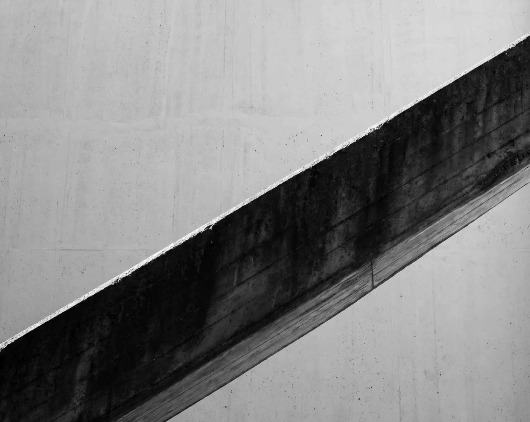 Diagonal concrete beam casting a shadow on a plain concrete wall in black and white.