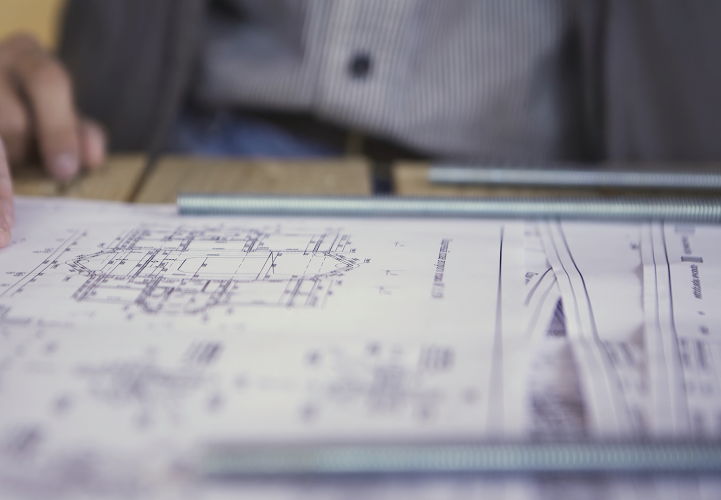 Blueprint with technical drawings on a table with metal rods alongside a blurred person.