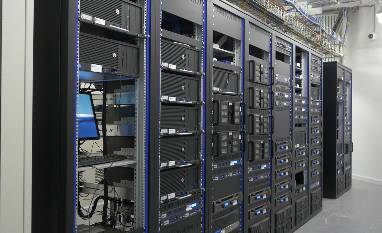 Row of black server racks with blinking blue lights and cables in a data center room.