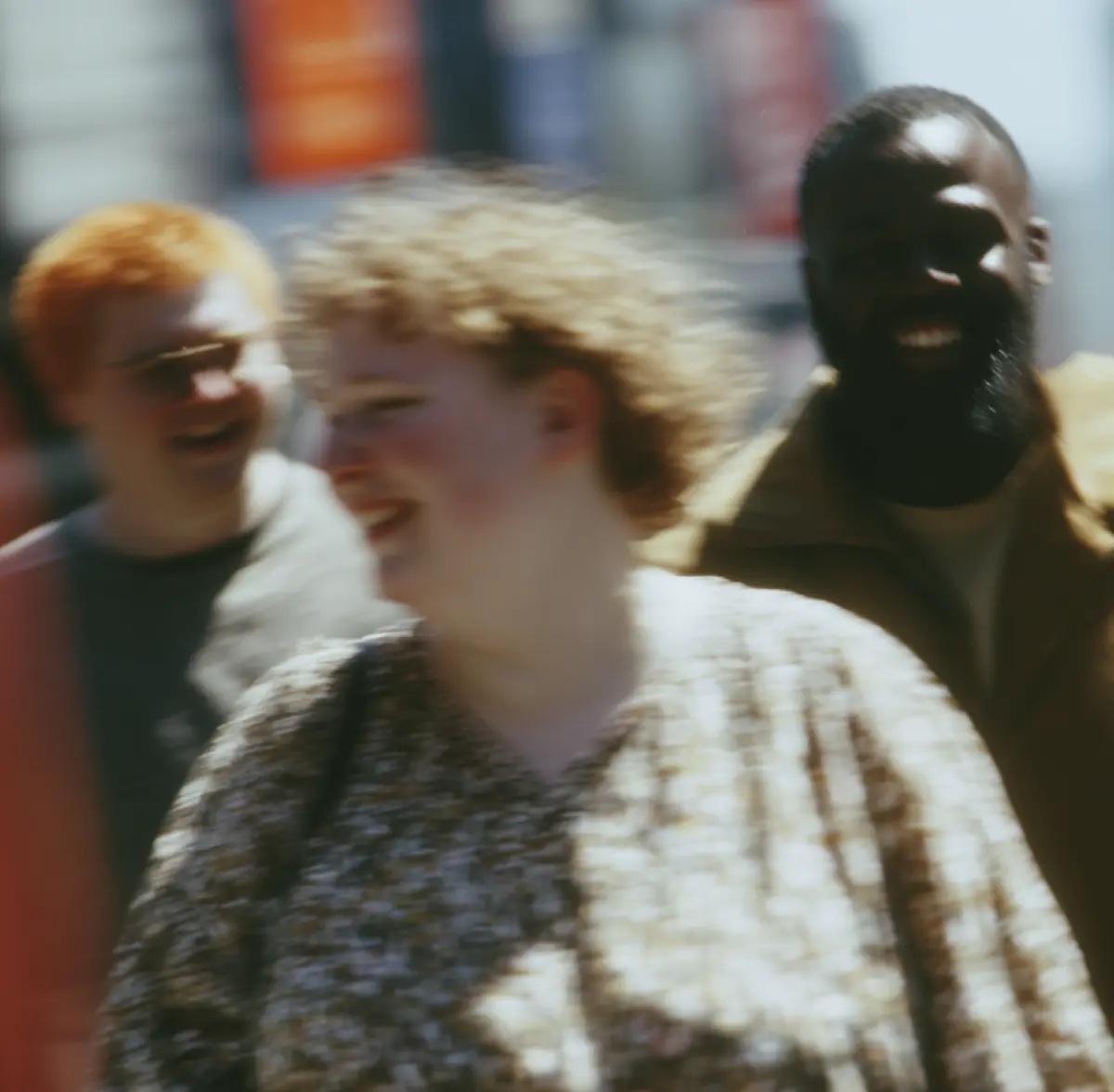 Three people smiling and walking outdoors on a sunny day, blurred image.