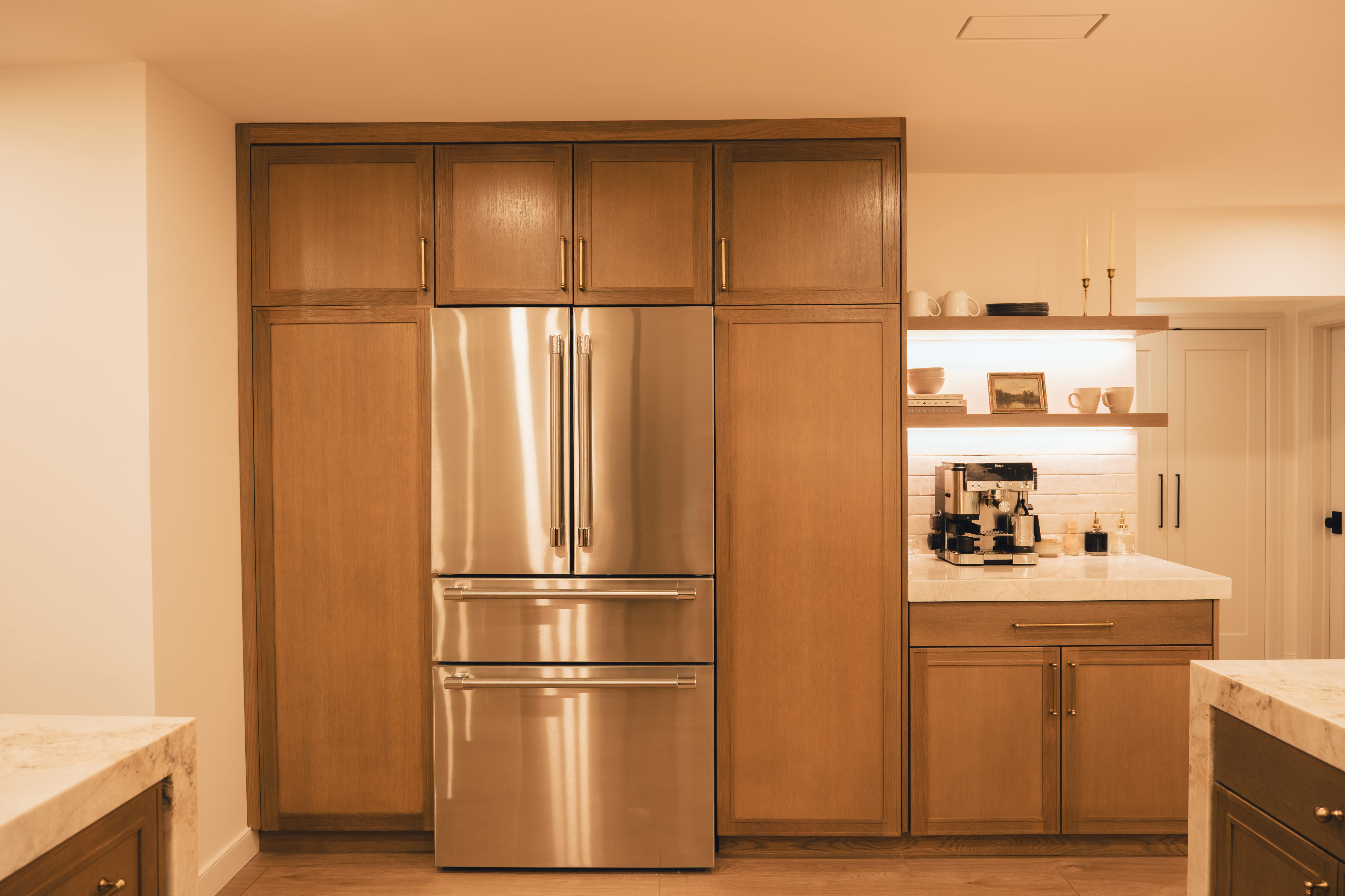Modern kitchen with stainless steel French door refrigerator surrounded by wooden cabinets and a coffee machine on the side.